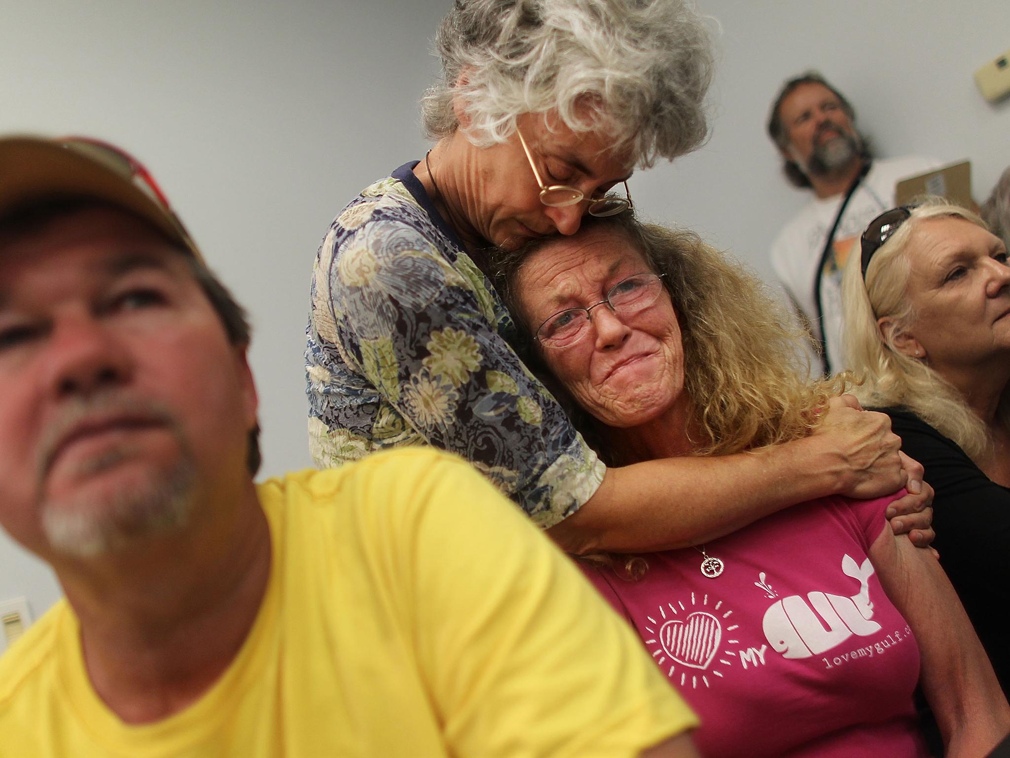 Lorrie Williams (centre) is hugged by oil pollution activist Riki Ott (top) as Bud Waltman (left) looks on at a meeting for Gulf Coast residents who have health problems possibly related to the BP oil spill