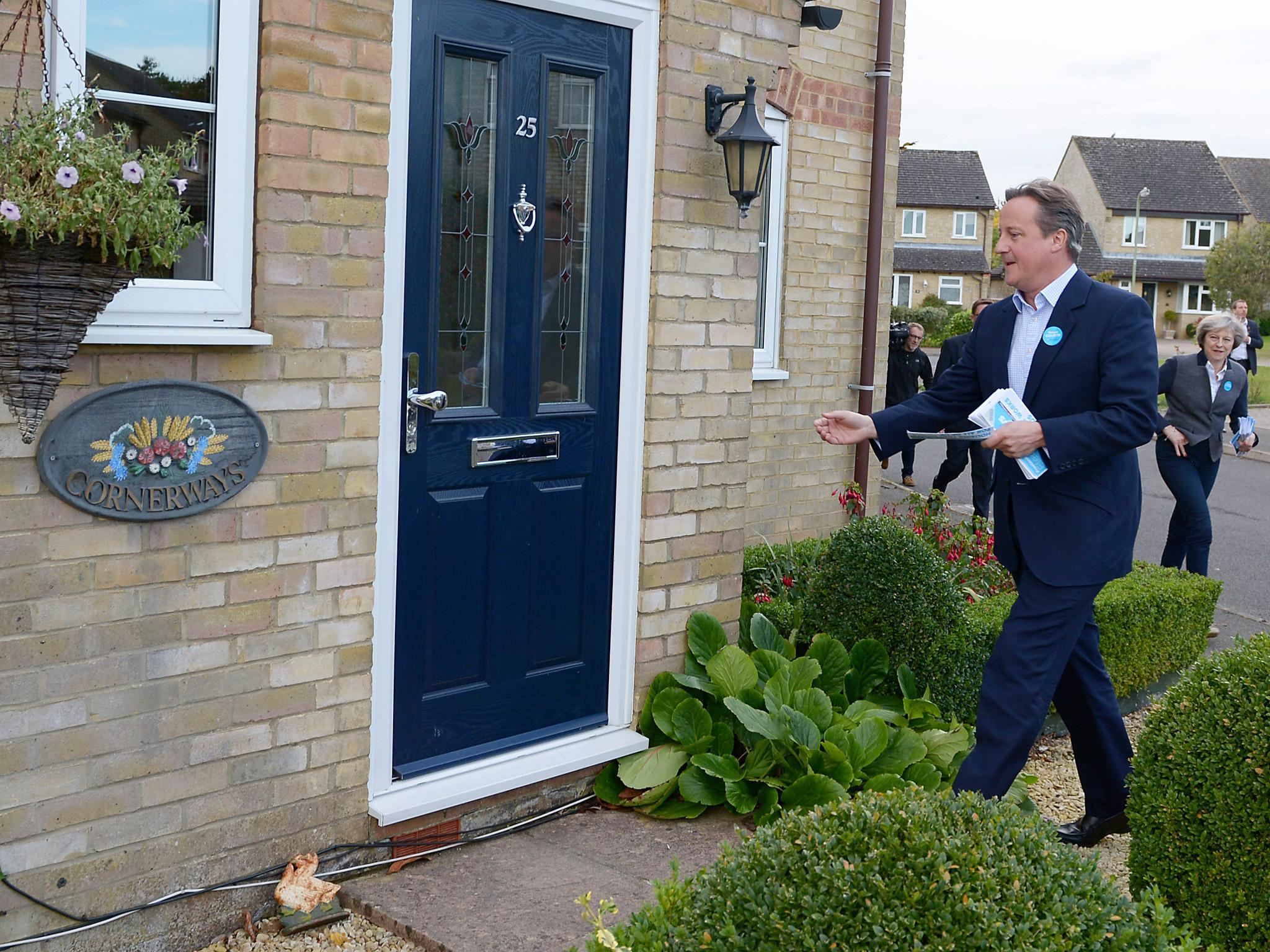 Former Prime Minister David Cameron (L) and British Prime Minister Theresa May (R) post fliers through doors with Robert Courts, the Conservative candidate for the Witney by-election