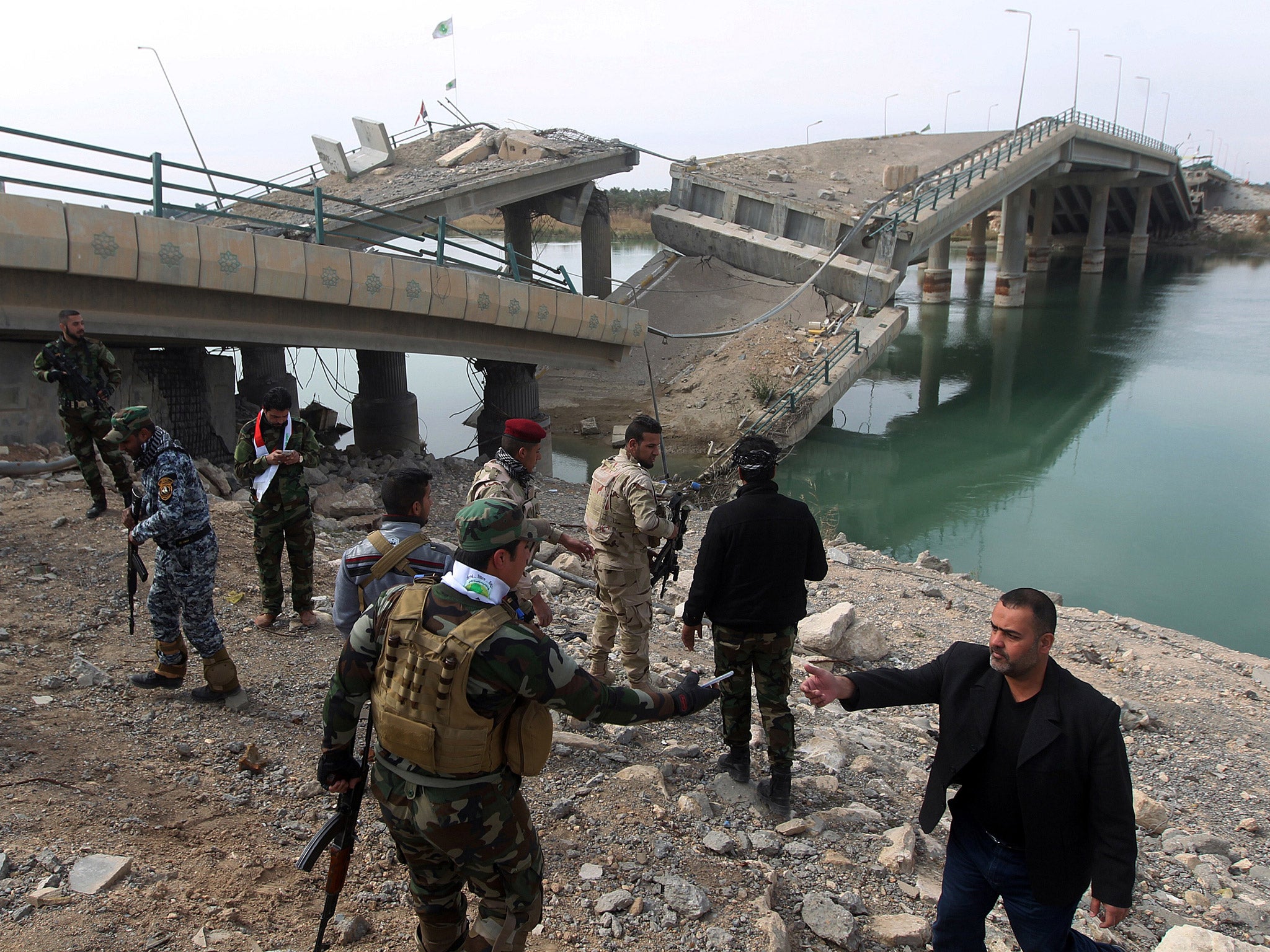 Volunteer Shiite fighters who support the government forces in the combat against the Islamic State (IS) group stand next to a destroyed bridge that connects the southwestern city of Fallujah with Baghdad on the oustkirts of the village of Fadhiliyah, which pro-government forces retook from IS militants