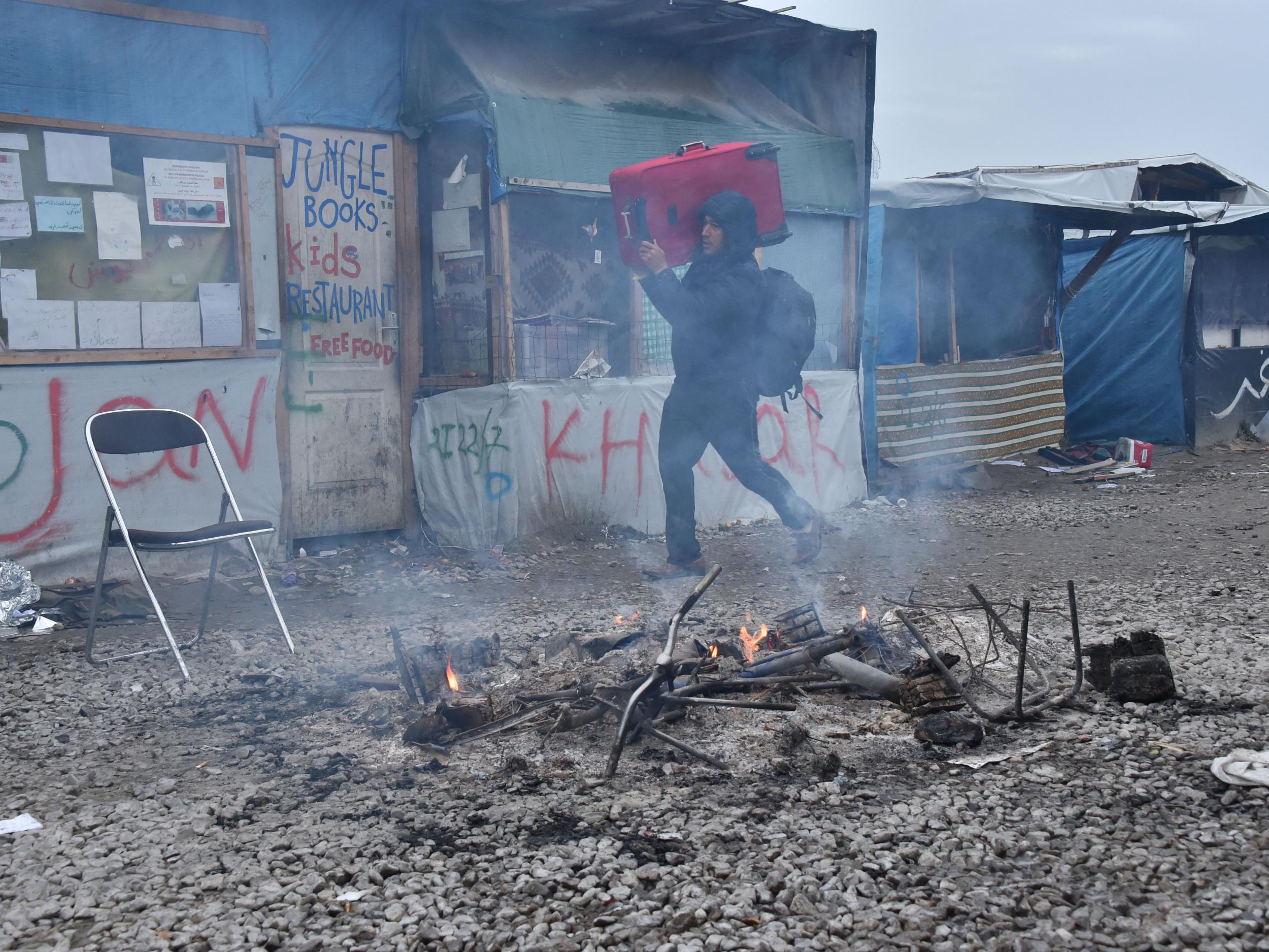 A person carries his luggage through the Jungle camp as he walks towards an official meeting point set by French authorities (Getty Images )