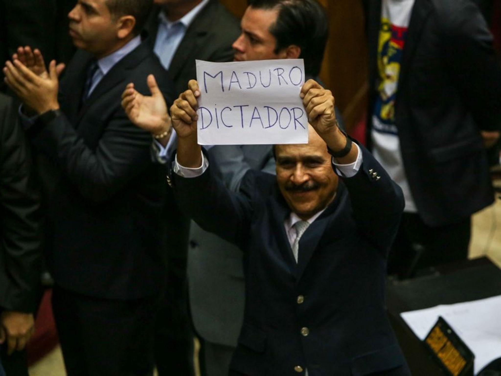 Opposition deputy Luis Silva holds a banner against Venezuelan President Nicolas Maduro, that says "Maduro dictator" during the debate in the National Assembly in Caracas, Venezuela, on 23 October, 2016