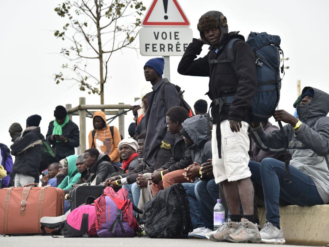 Refugees with their luggage wait to leave the Jungle migrant camp in Calais