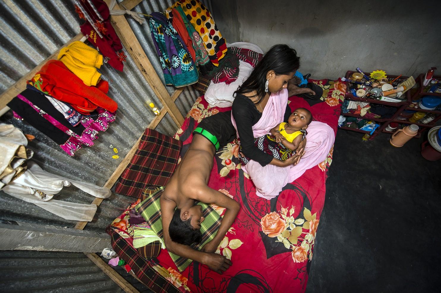 Kajol with her 6-month-old baby Mehedi and a customer on her bed