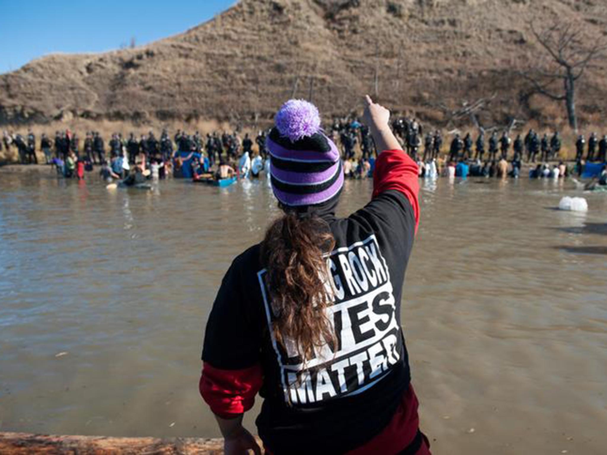 People yell at police officers standing on the opposite shore of a river during a protest against the building of a pipeline on the Standing Rock Indian Reservation