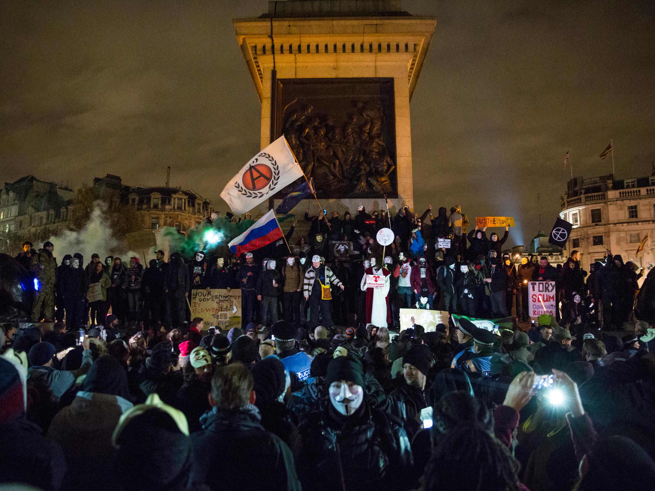 Masked protesters hold placards and wave flags as they stand on and around Nelson's Column (Getty Images )