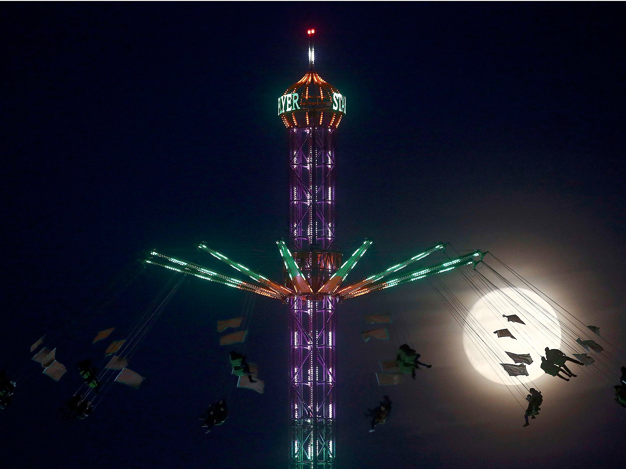 People on a funfair ride are silhouetted against the moon in London