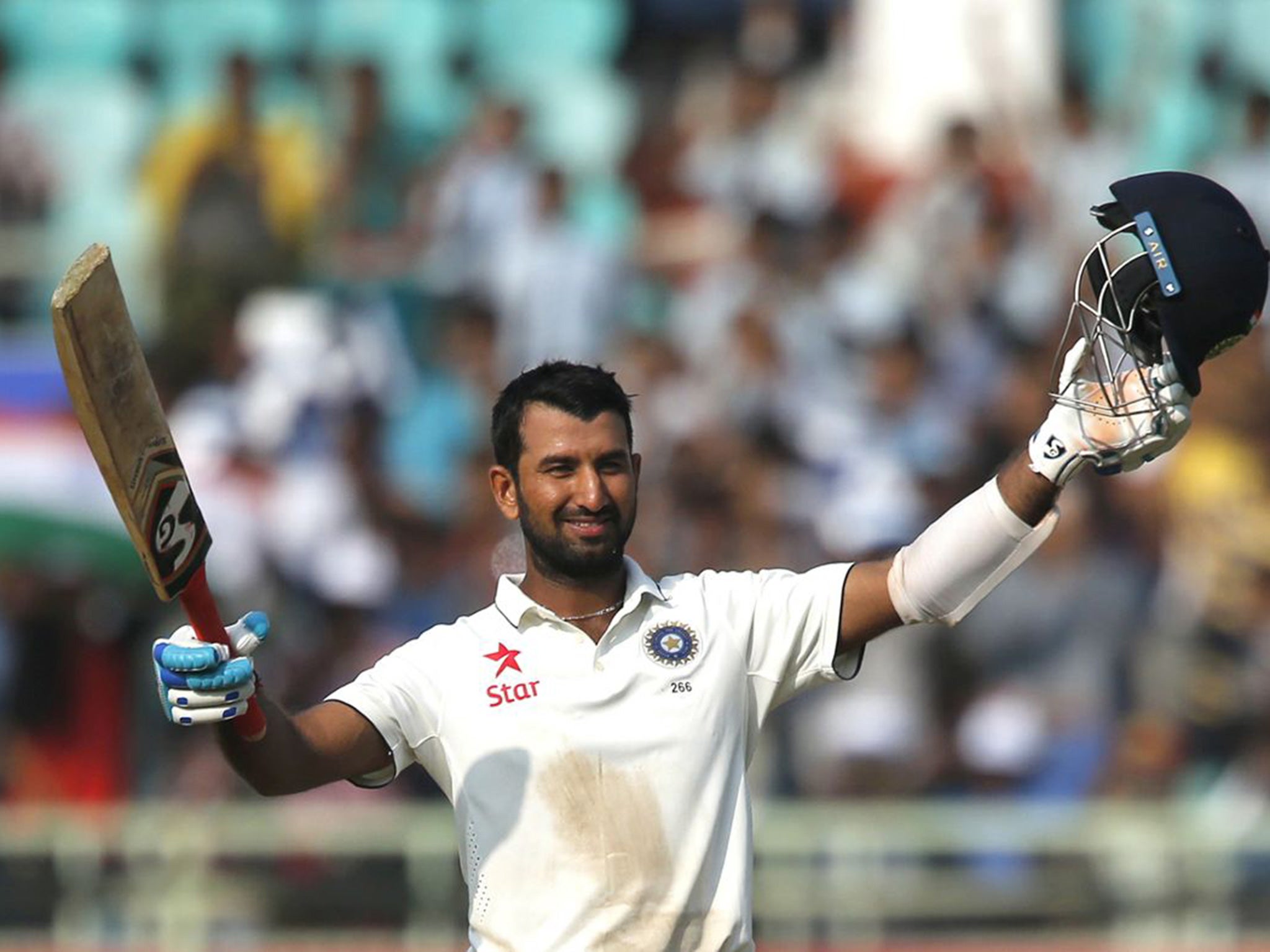 Pujara raises his bat and helmet to celebrate reaching his century