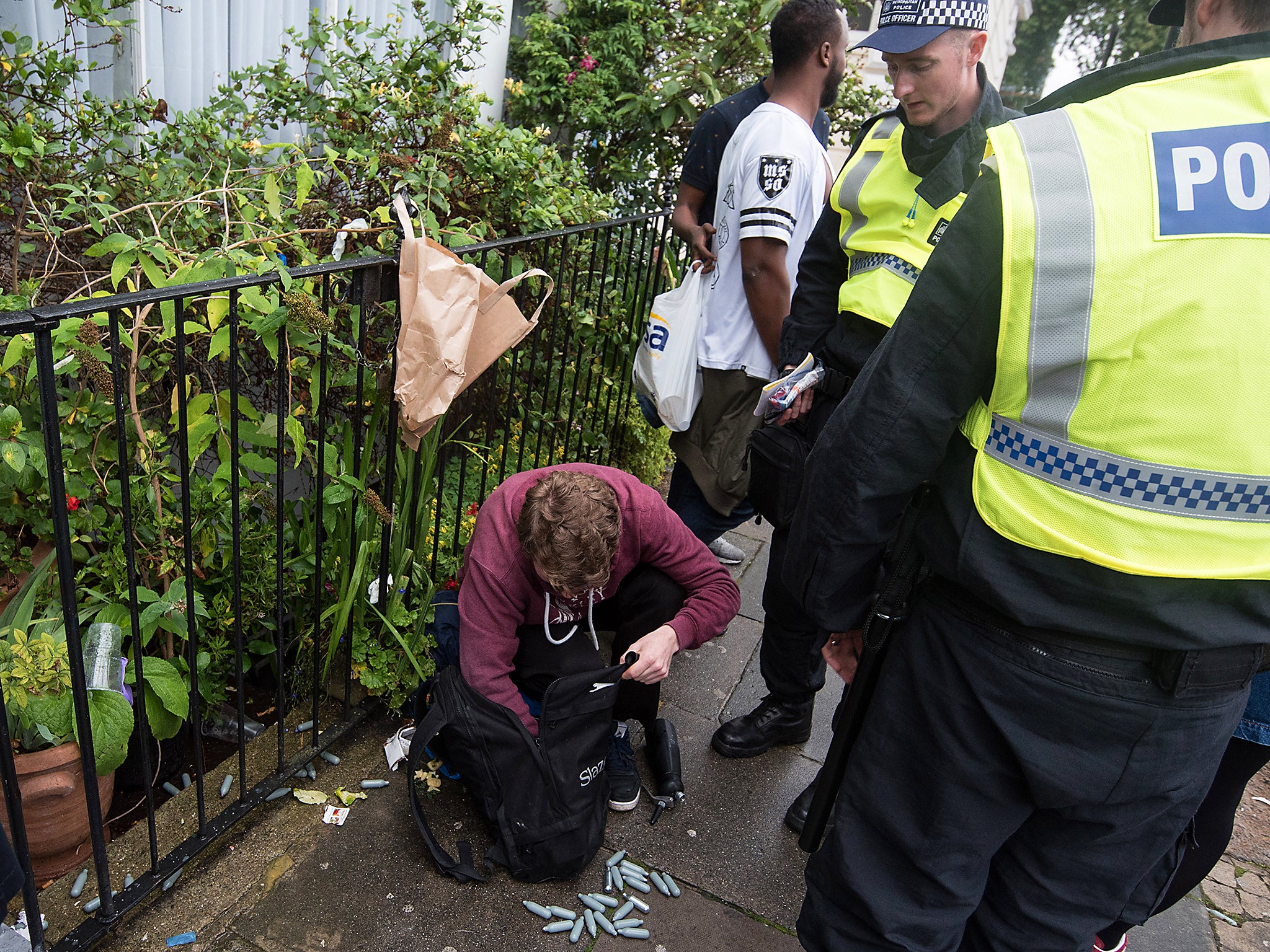 Police officers inspect the content of a man's rucksack containing canisters of nitrous oxide