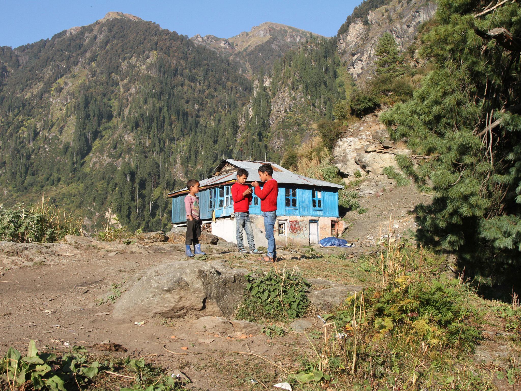 Children play in front of a mountain home that stands alone at the upper-end of Malana