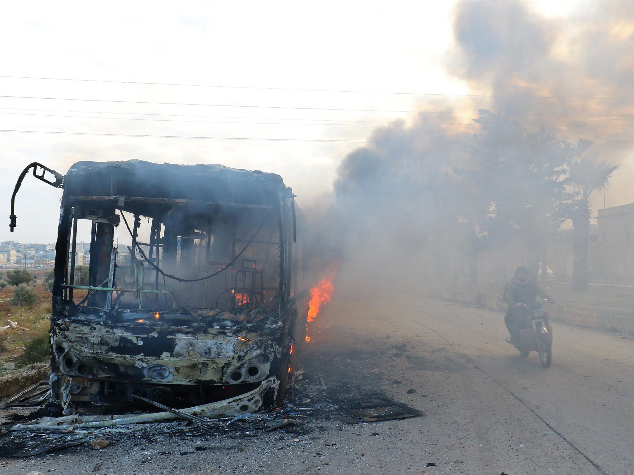 A man on a motorcycle drives past burning buses while en route to evacuate ill and injured people from the besieged Syrian villages of al-Foua and Kefraya, after they were attacked and burned, in Idlib province, Syria