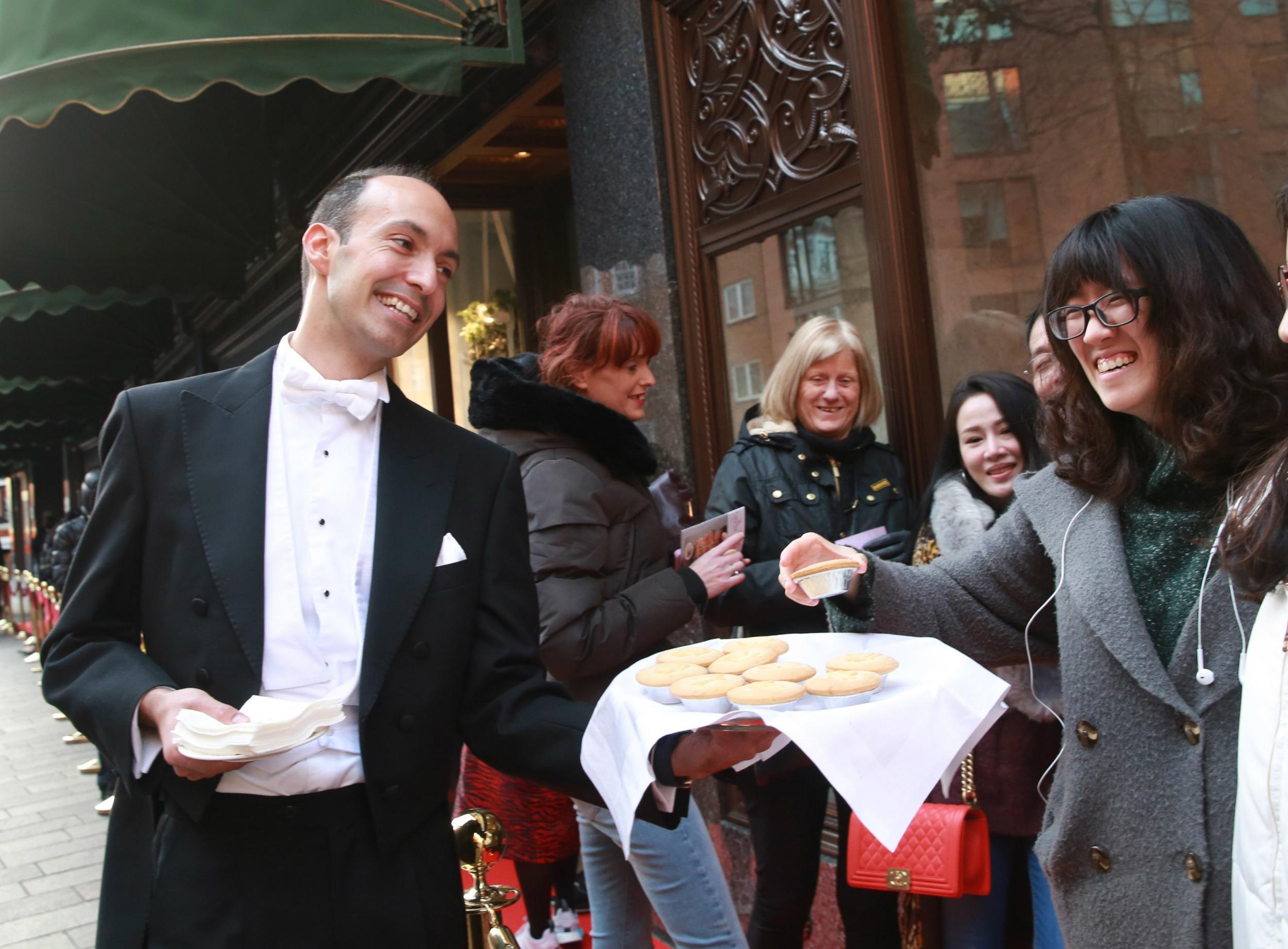 Harrods butlers serve mince pies, tea and coffee to queuing crowds ahead of the opening of the Harrods winter sale in Knightsbridge, London