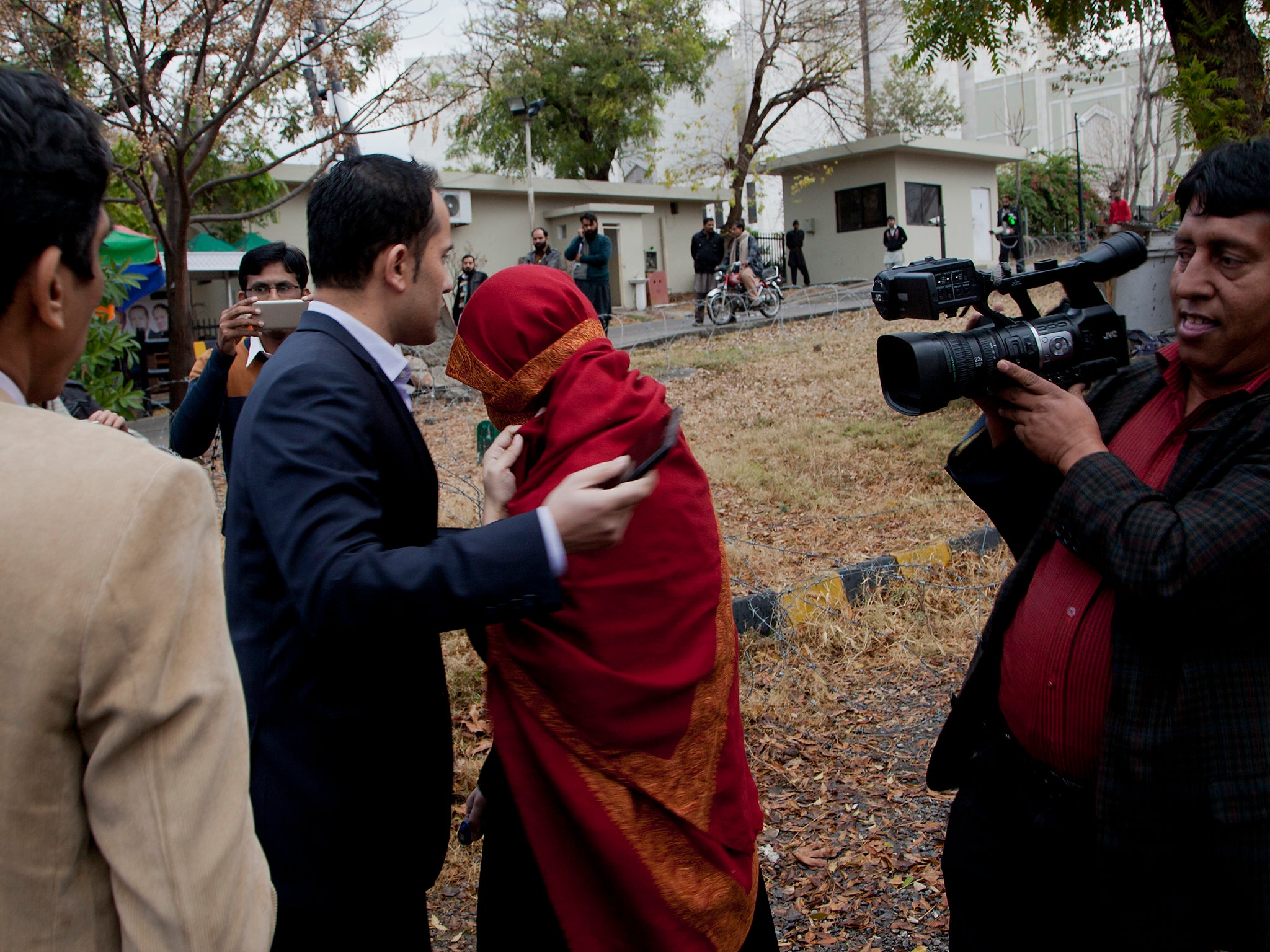 The wife, in red shawl, of a judge who allegedly tortured her maid, avoids the waiting media outside the Supreme Court building in Islamabad