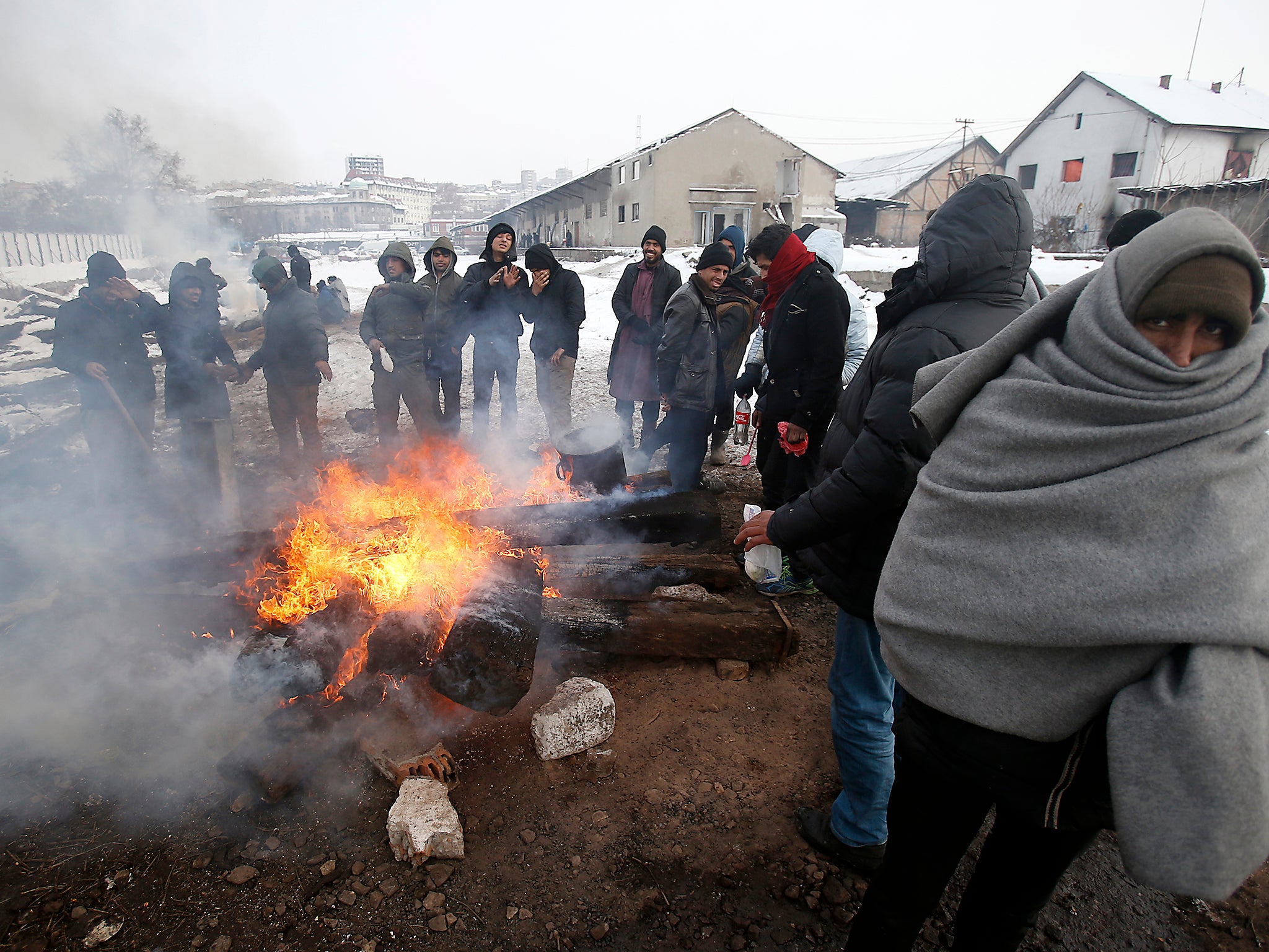 Migrants warm themselves by the fire in front of an abandoned warehouse in Belgrade