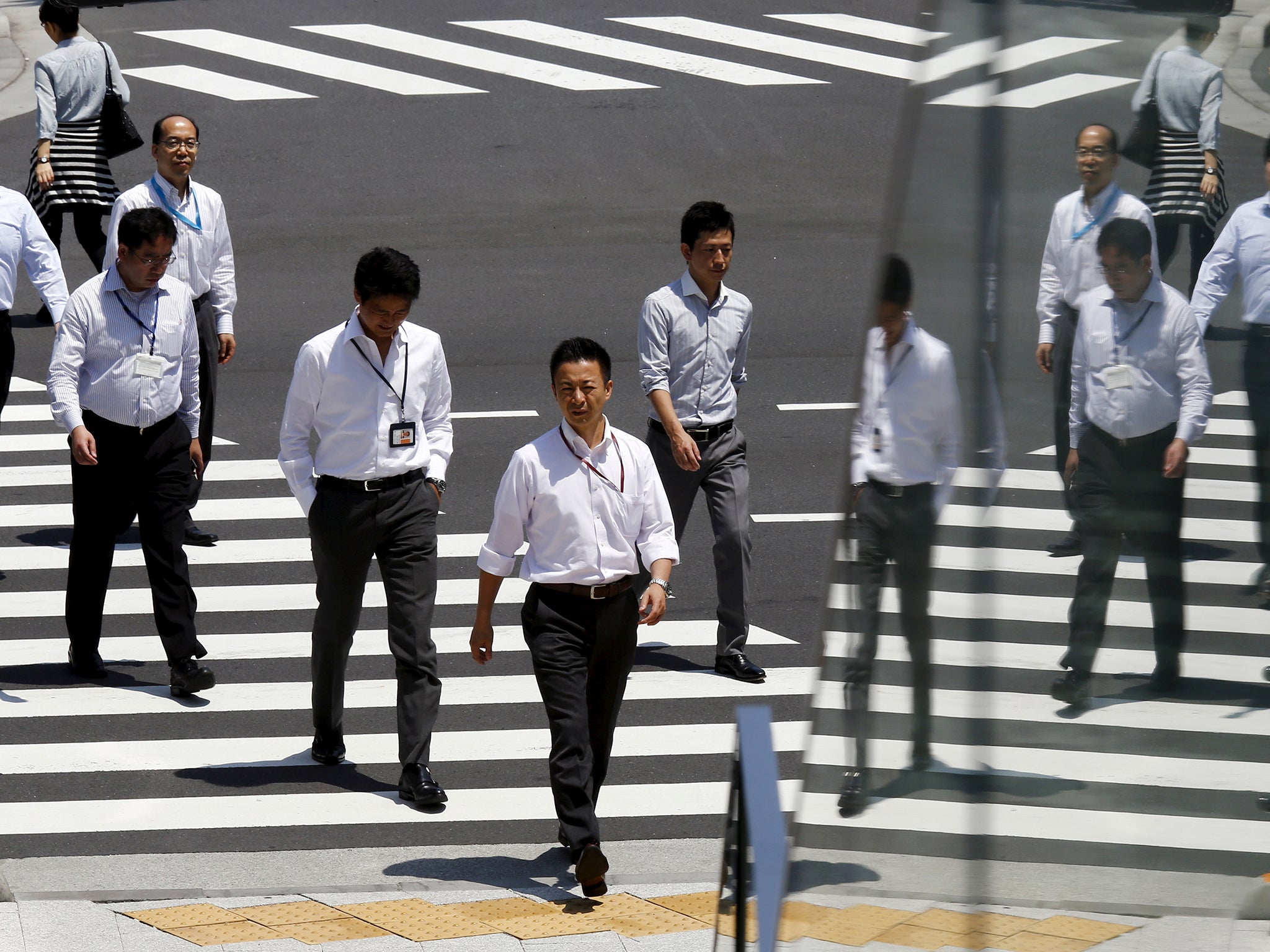 Office workers are reflected in a glass railing as they cross street during lunch hour in Tokyo