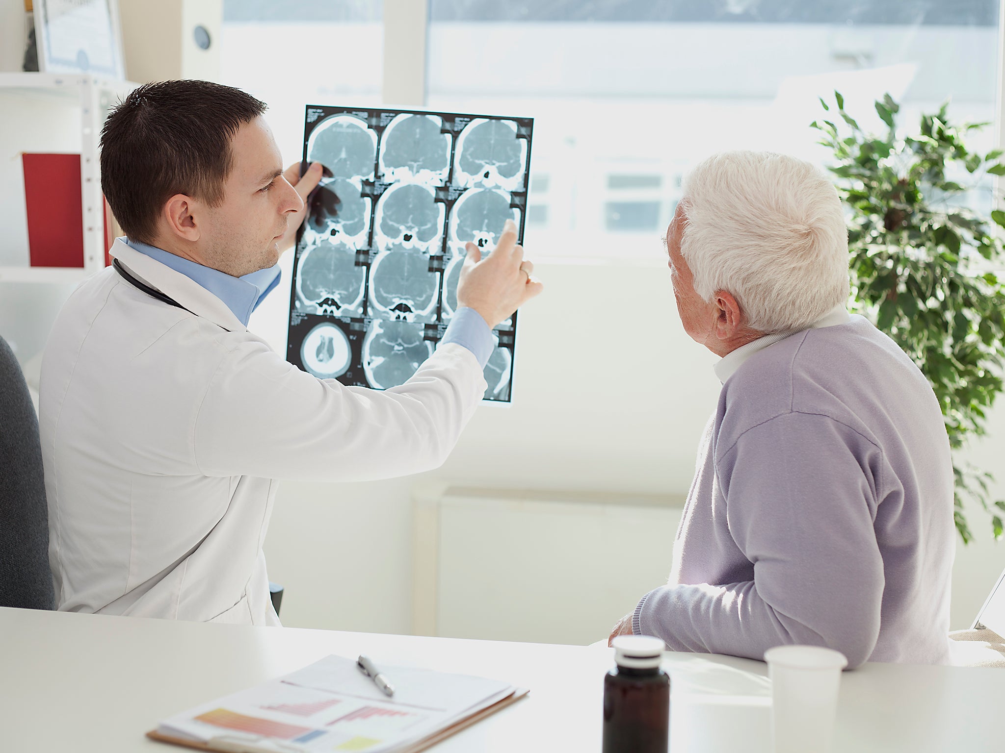 A doctor analyses the CT scan of a human skull with a senior man inside a doctor’s office.(Getty)