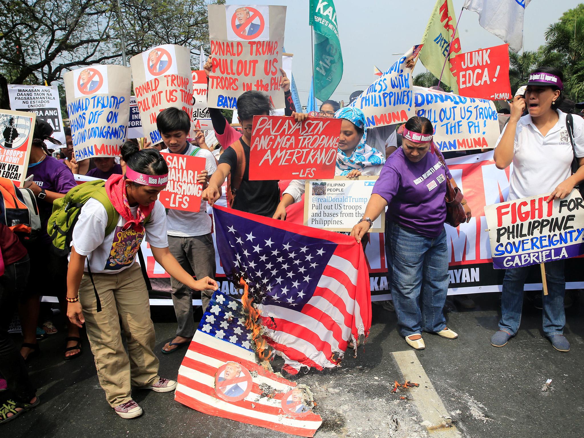 Protesters burn a U.S. flag and a mock flag with pictures of U.S. President-elect Donald Trump outside the U.S. embassy in metro Manila, Philippines