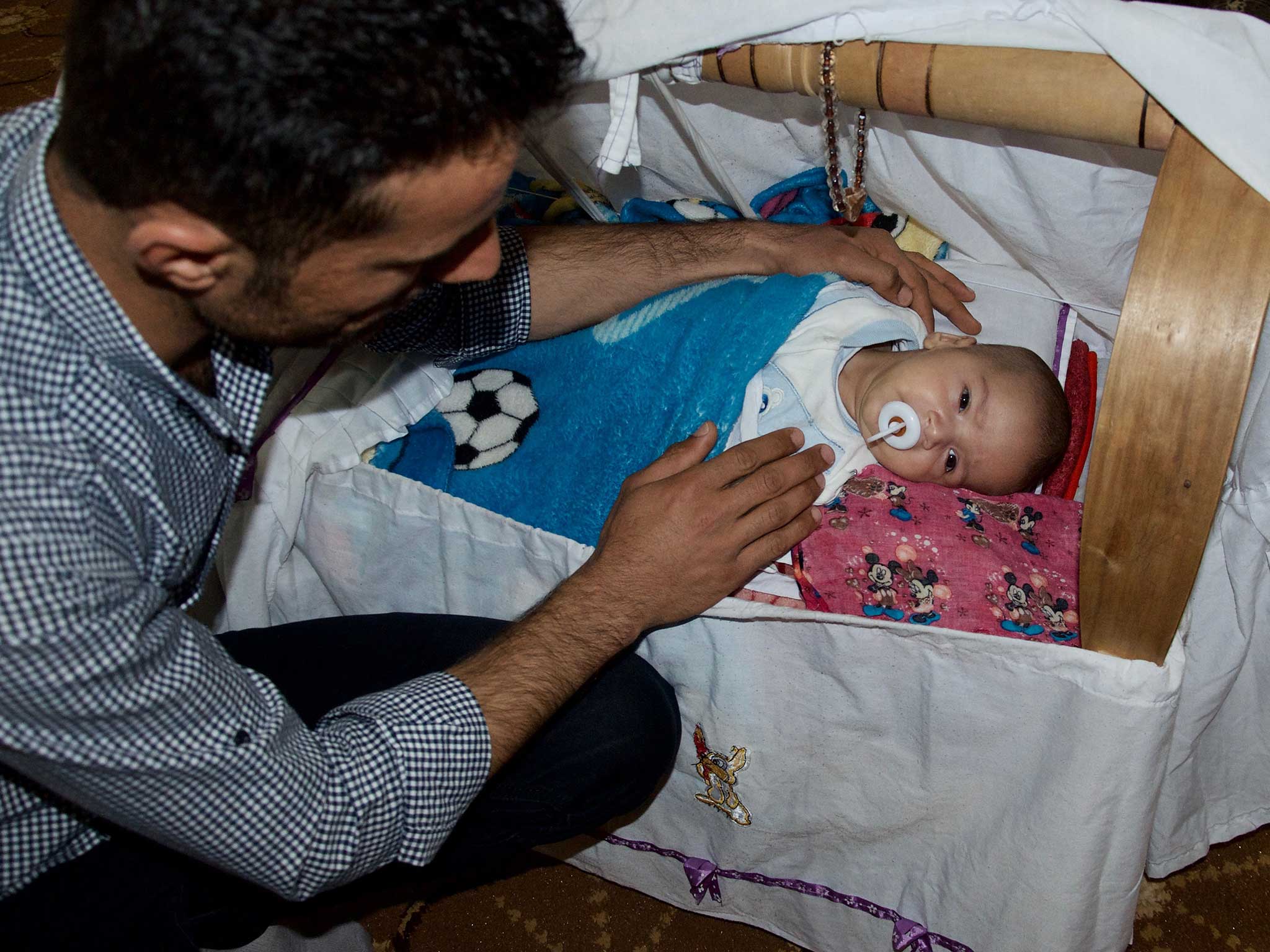 Hassan Jamil, a Kurdish peshmerga fighter, with his infant son in his living room in Chrra, a town in the Kurdistan region of Iraq. The baby's name is Trump