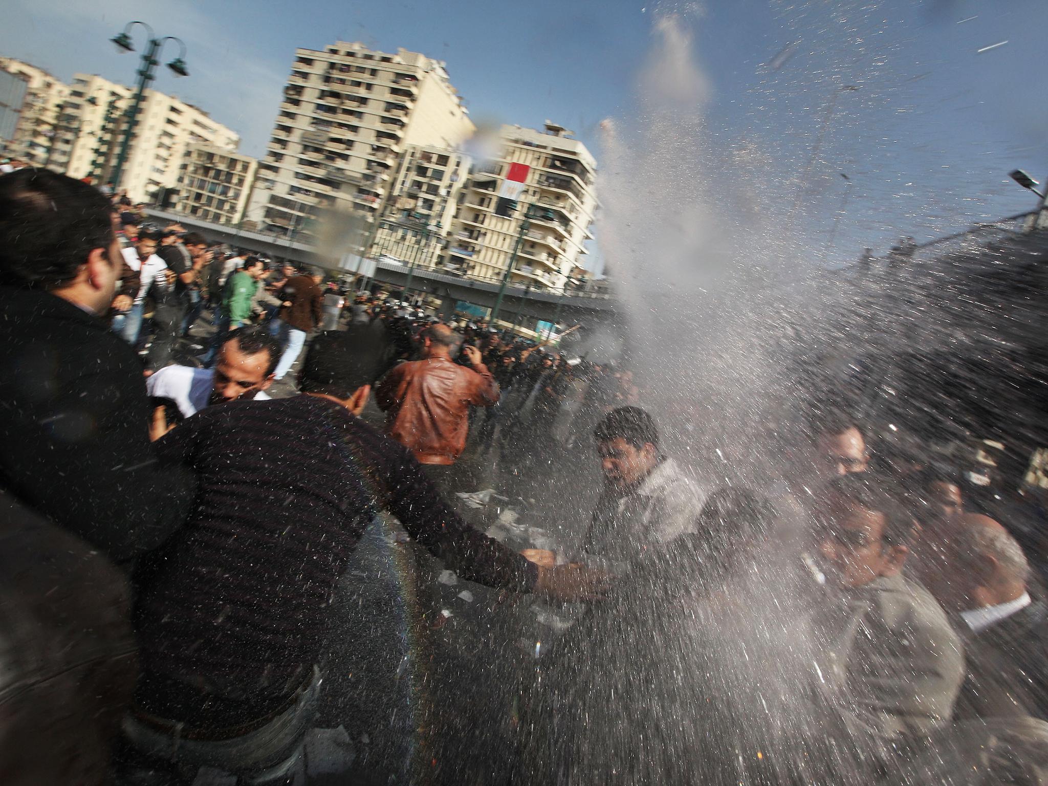 Arab Spring protestors are hit by a water cannon in front of The l-Istiqama Mosque, as they're watched by riot police in Giza