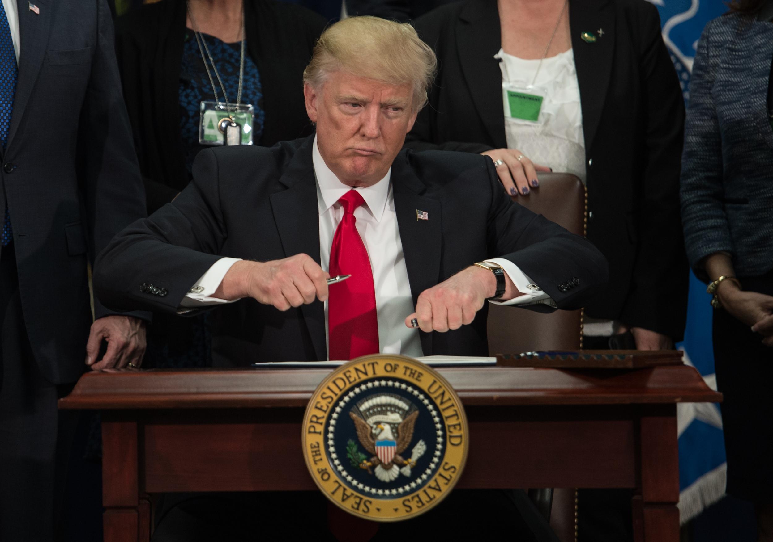 Donald Trump takes the cap off a pen to sign an executive order