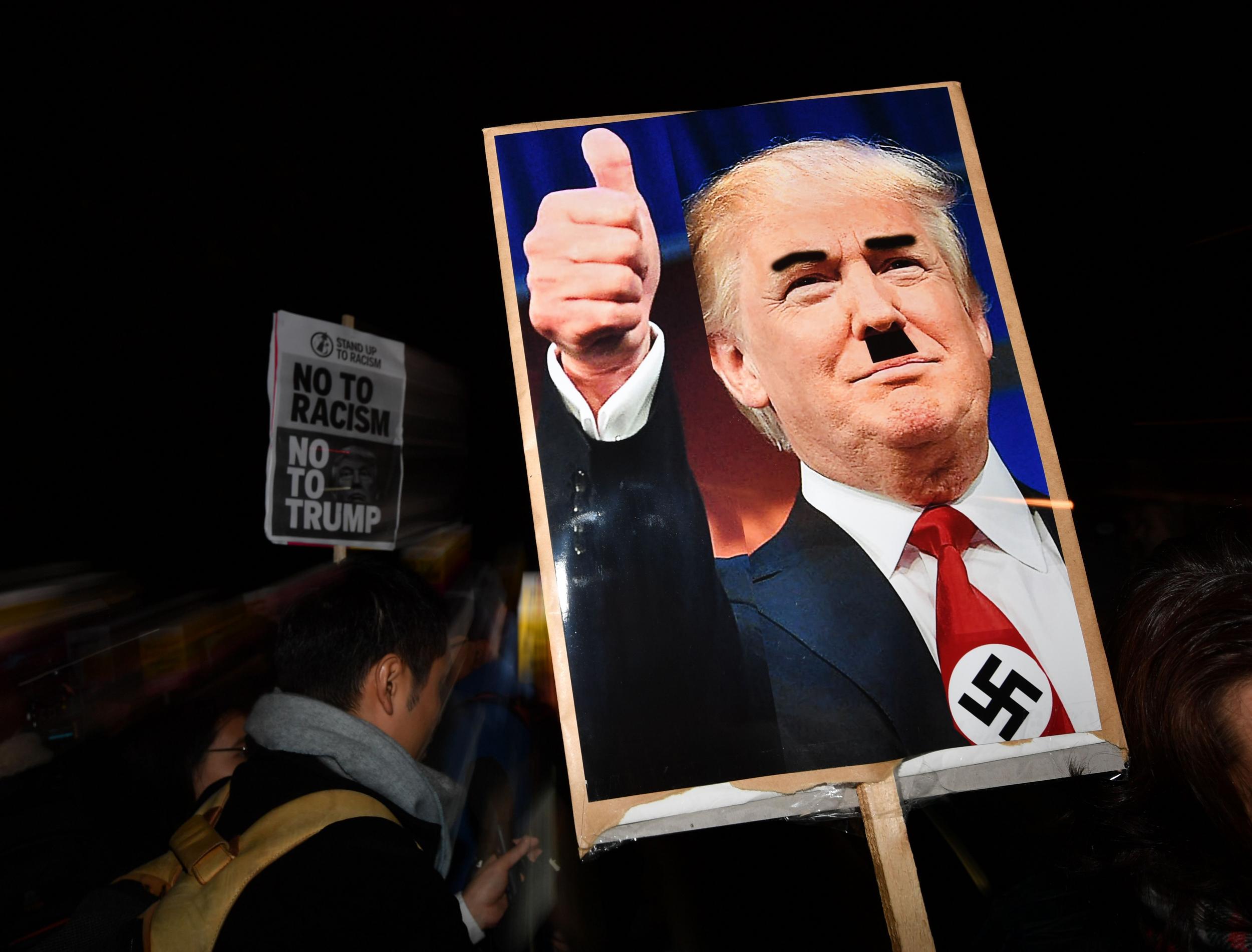 A demonstrator holds a placard showing a picture of US President-elect Donald Trump modified to add a swastika and an Adolf Hitler-style moustache during a protest outside the US Embassy in London