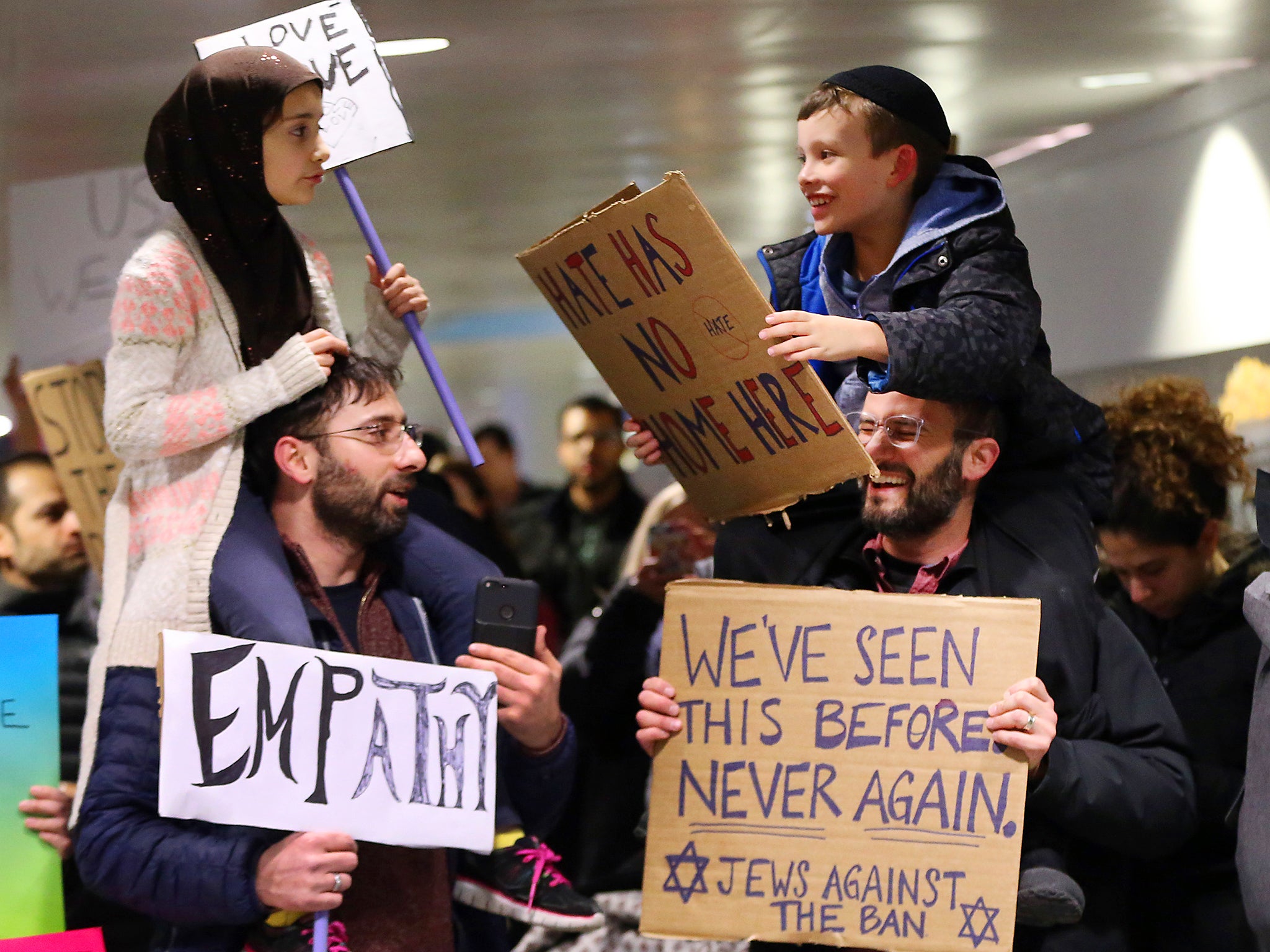 Yildirim, 7, left, sits on her father, Fatih, of Schaumburg, and Adin Bendat-Appell, 9, right, sits on his father, Rabbi Jordan Bendat-Appell, of Deerfield, during a protest at O'Hare International Airport in Chicago