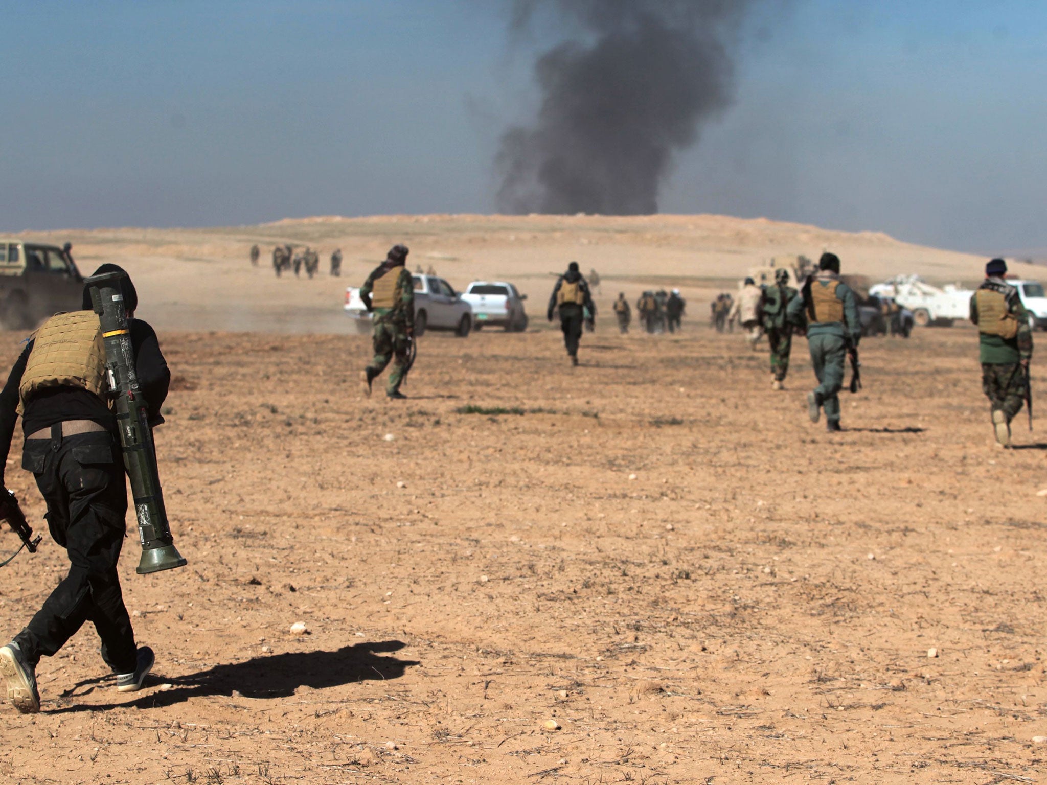 Smoke billows in the background as Iraqi forces, supported by the Hashed al-Shaabi