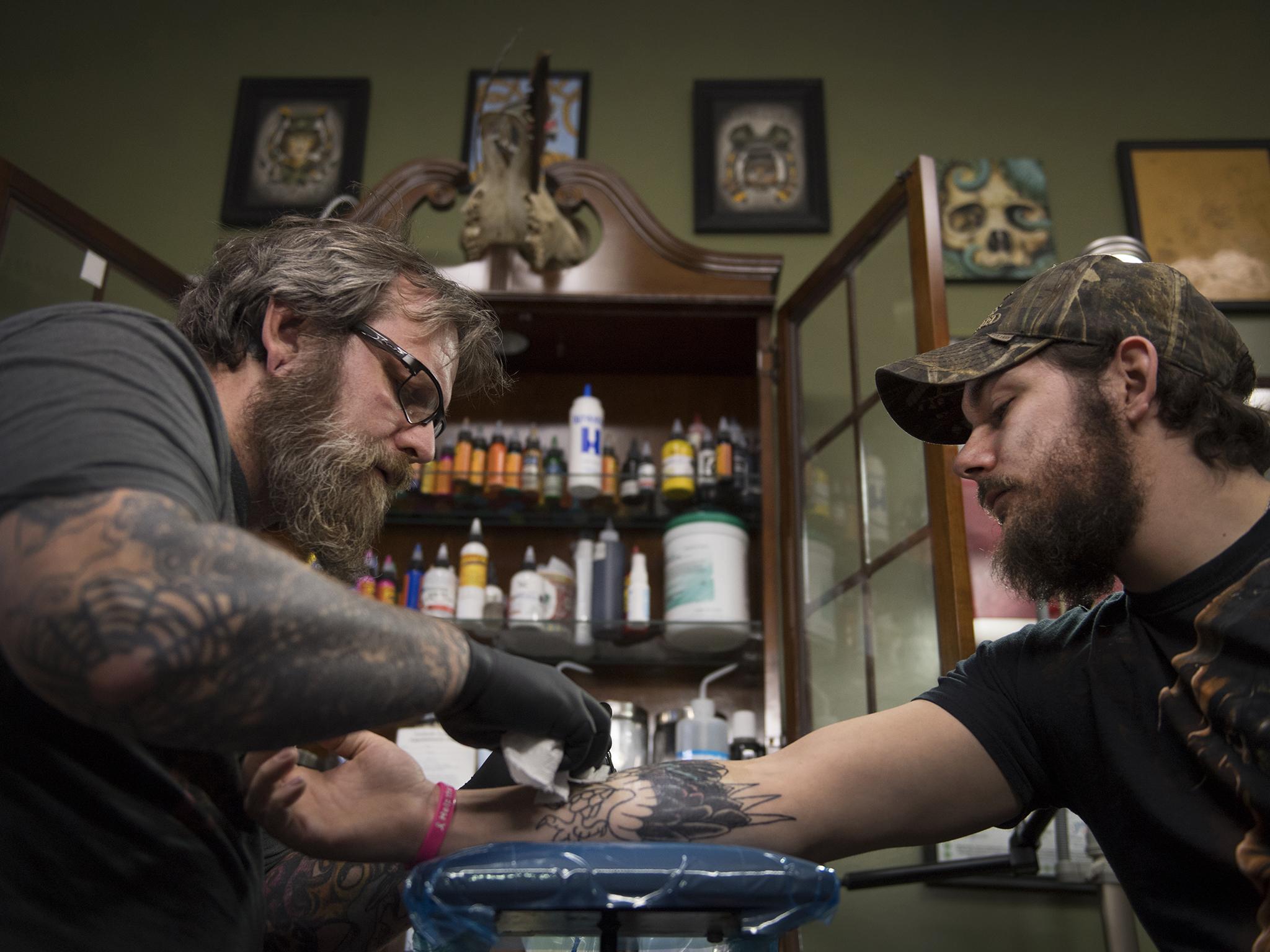 Tattoo parlor owner Dave Cutlip, left, creates an eagle design to cover a tattoo of a Confederate flag on the arm of Randy Stiles, 25, in Brooklyn Park, Maryland