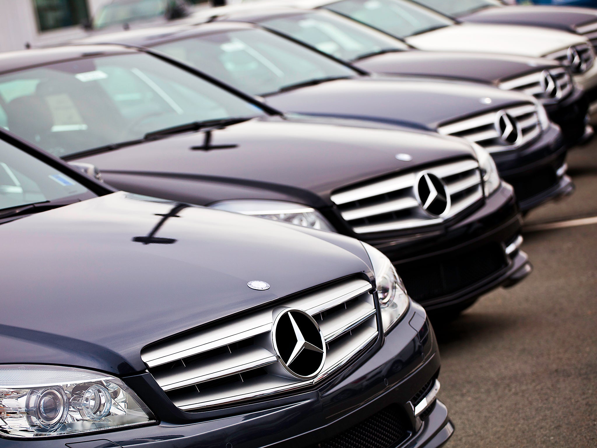 Various Mercedes Benz vehicles in a row at a Mercedes/Smart dealership. Identical models of Mercedes C-Class vehicles