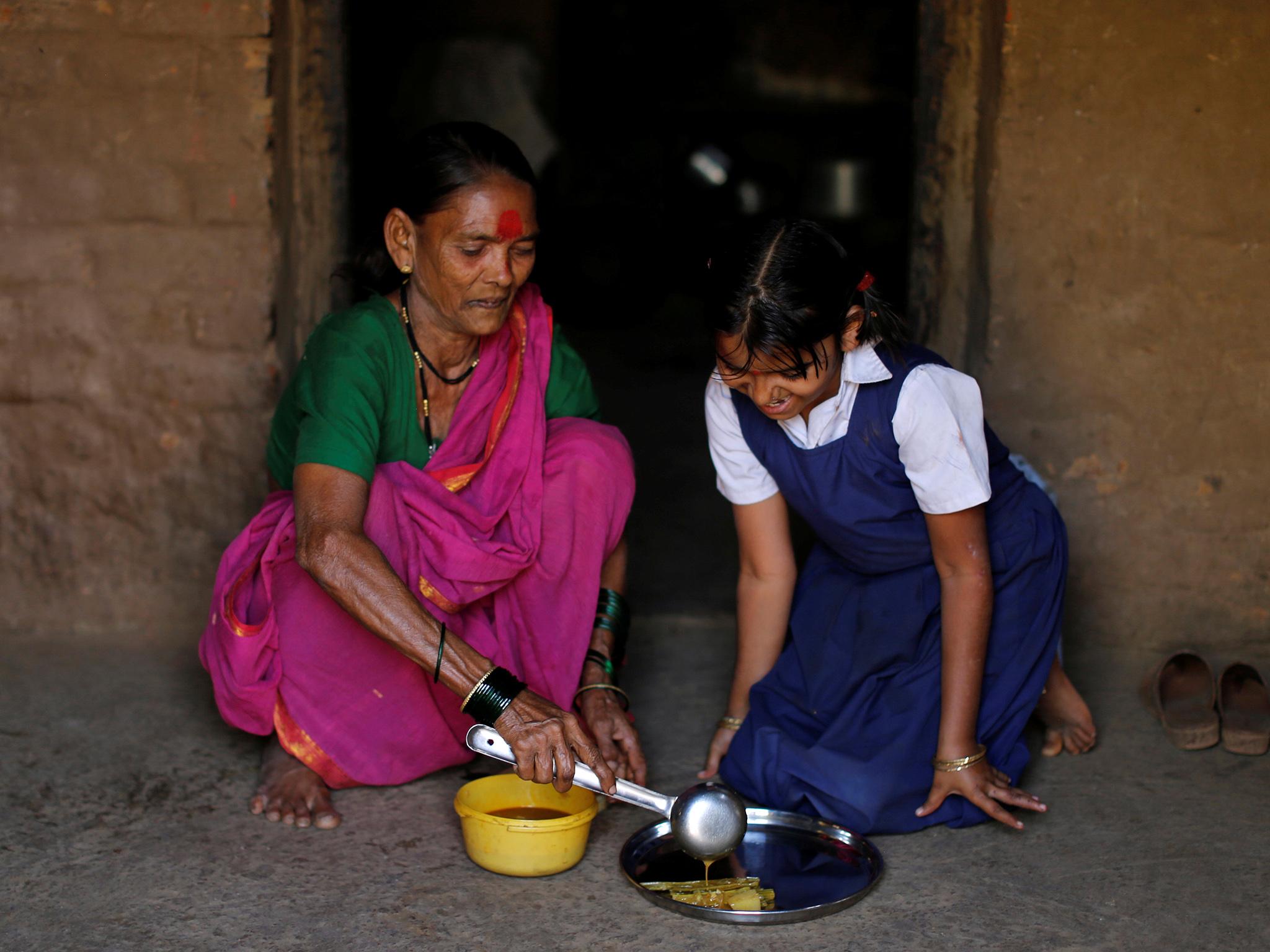 Drupada Pandurangkedar, 70, who studies at Aajibaichi Shaala (Grandmothers' School), serves her granddaughter Namita Thackrey lunch inside their house in Fangane village, India