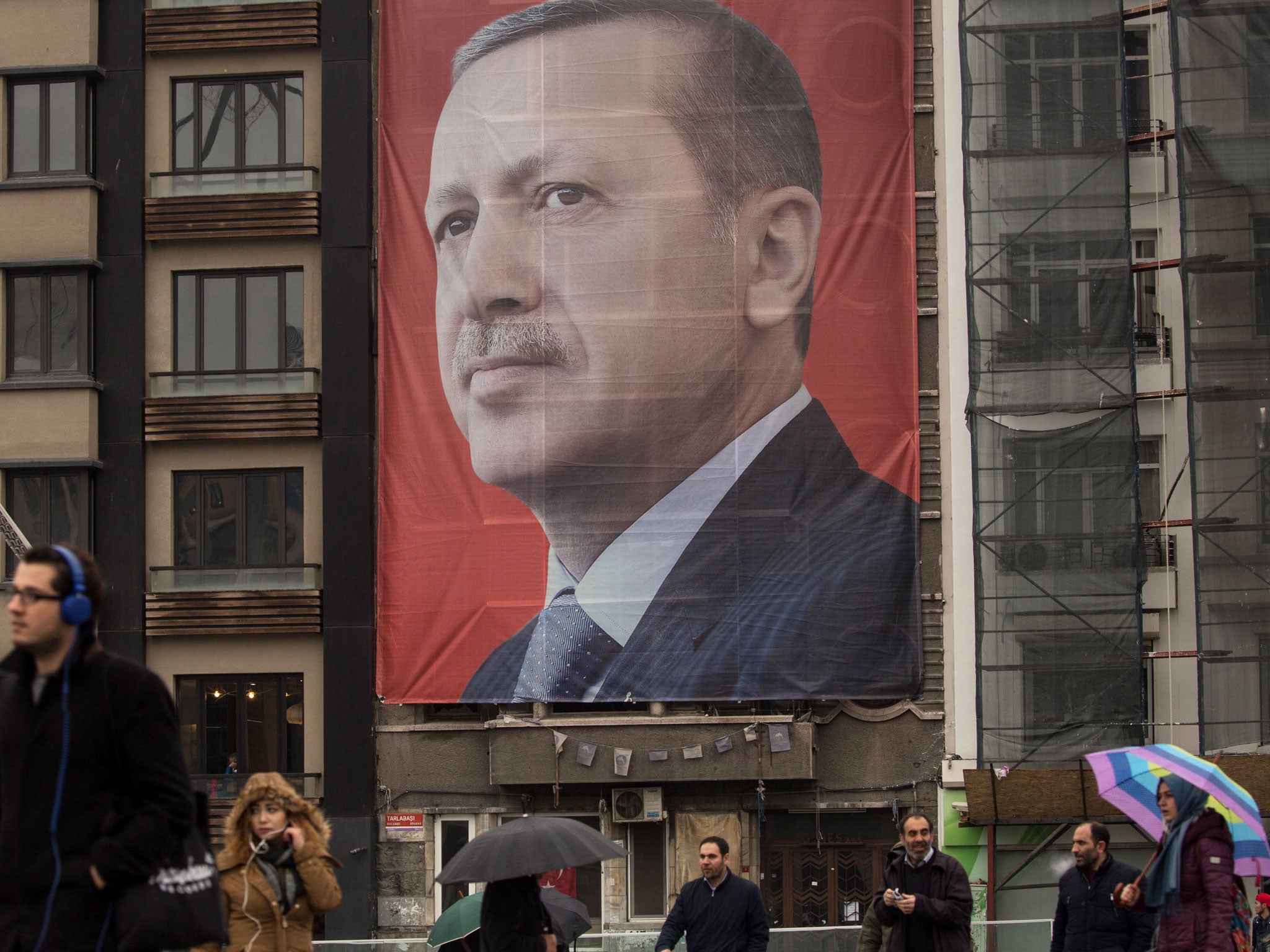 People walk past a large banner showing the portrait of Turkish President Recep Tayyip Erdogan in Taksim Square