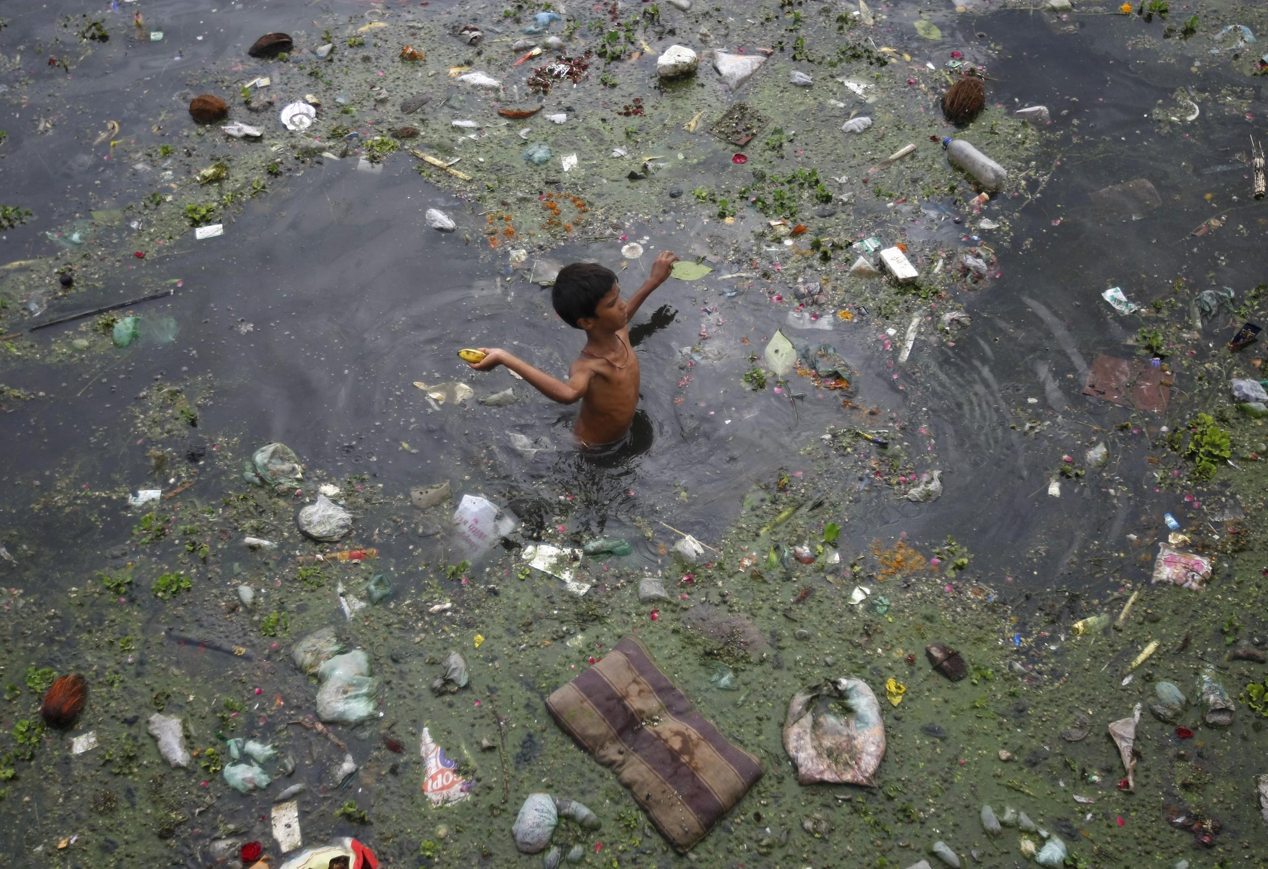 A boy throws a banana after collecting it from the polluted waters of River Sabarmati in Ahmedabad, India