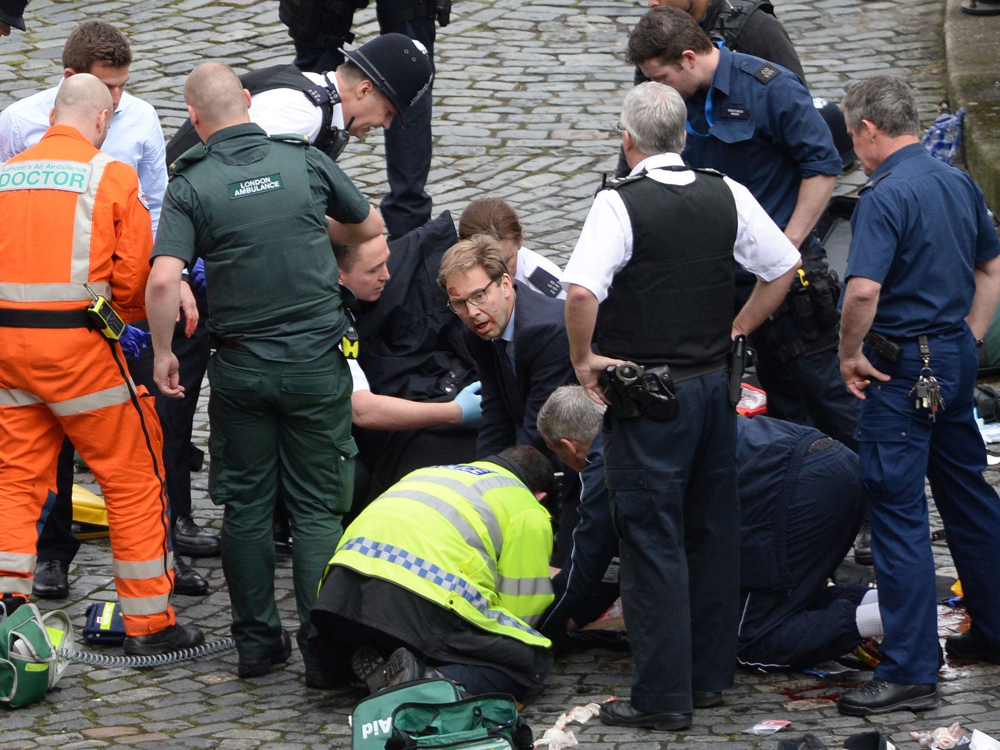 Conservative MP Tobias Ellwood (centre) helps emergency services attend to a police officer outside the Palace of Westminster