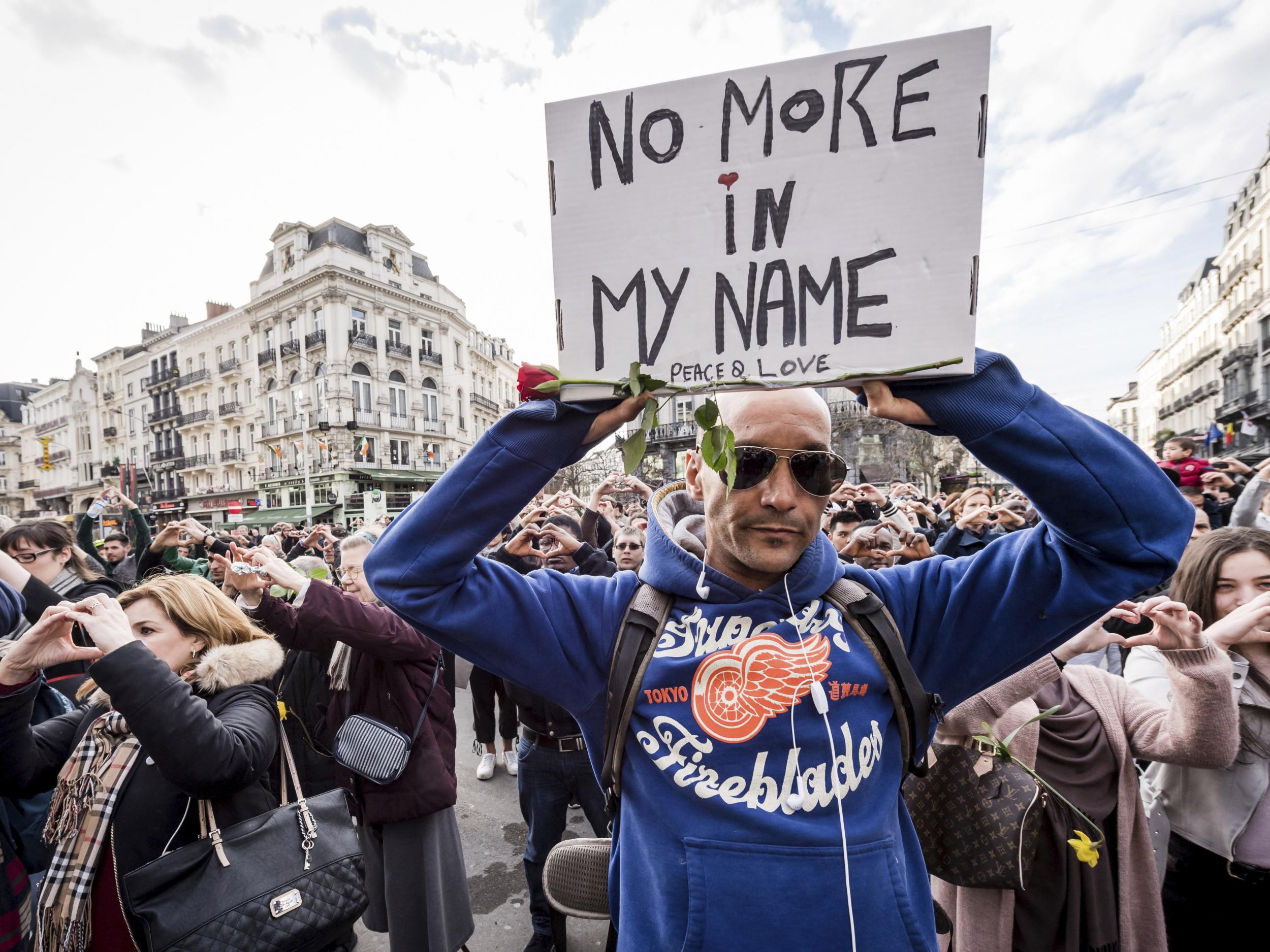 A man holds up a sign as he stands for a moment of silence at the Bourse during the one-year anniversary for Brussels attacks victims