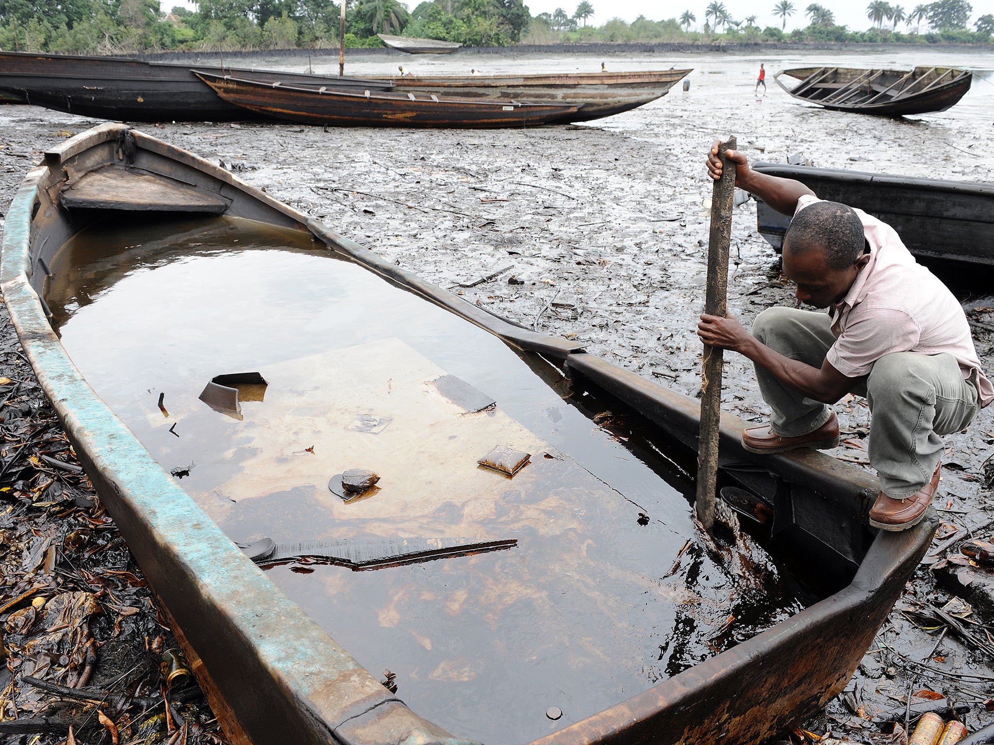 A man from the Bodo community, in Ogoniland, tries to separate with a stick the crude oil from water in a boat after waterways were polluted by oil spills attributed to Shell equipment failure.