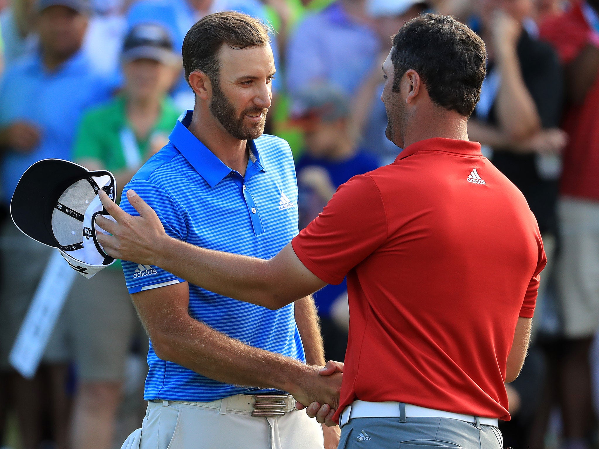 Johnson shakes hands with Jon Rahm after winning their match on the 18th green