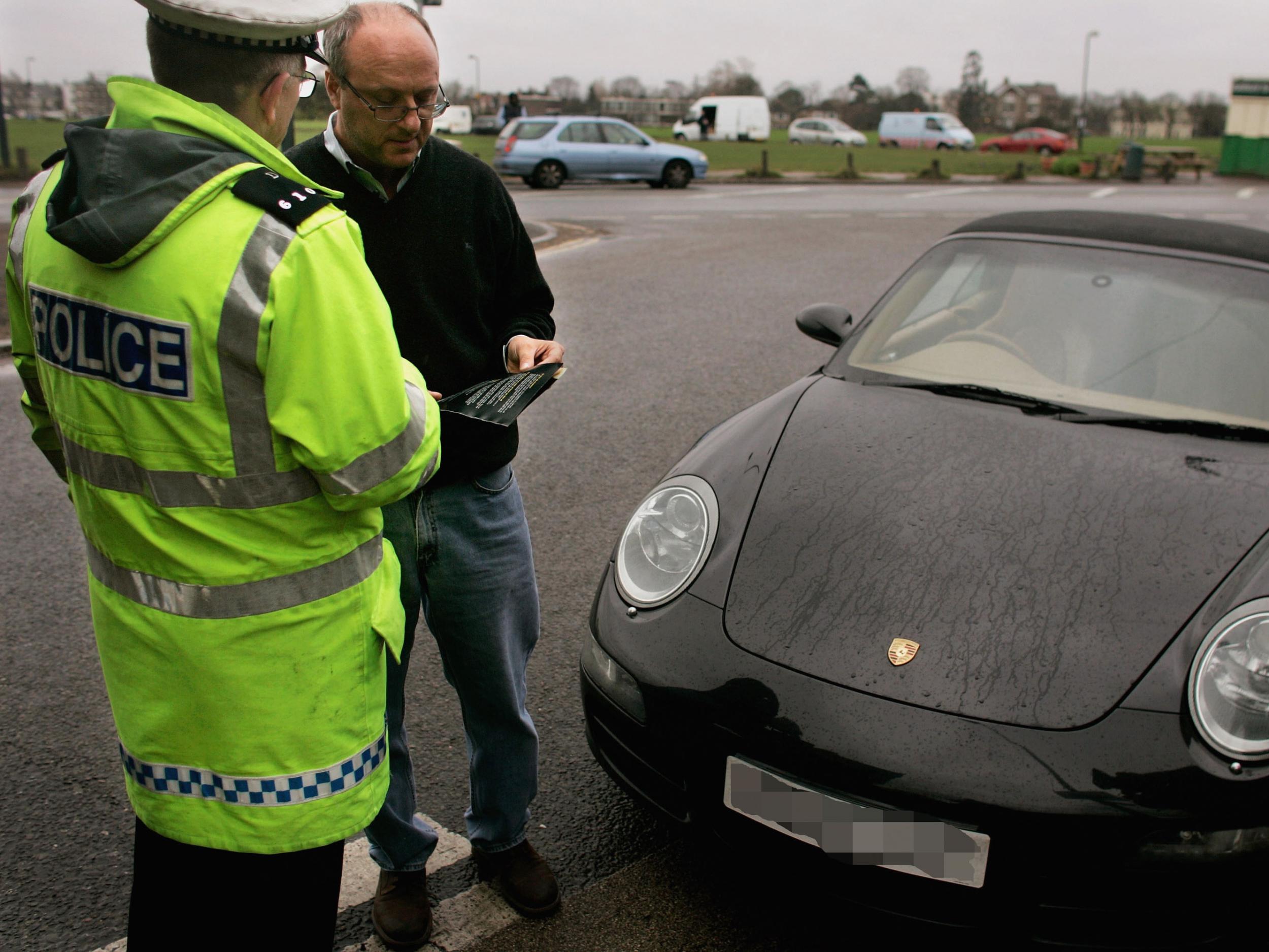 A Police officer hands a leaflet to a driver caught using his telephone whilst driving