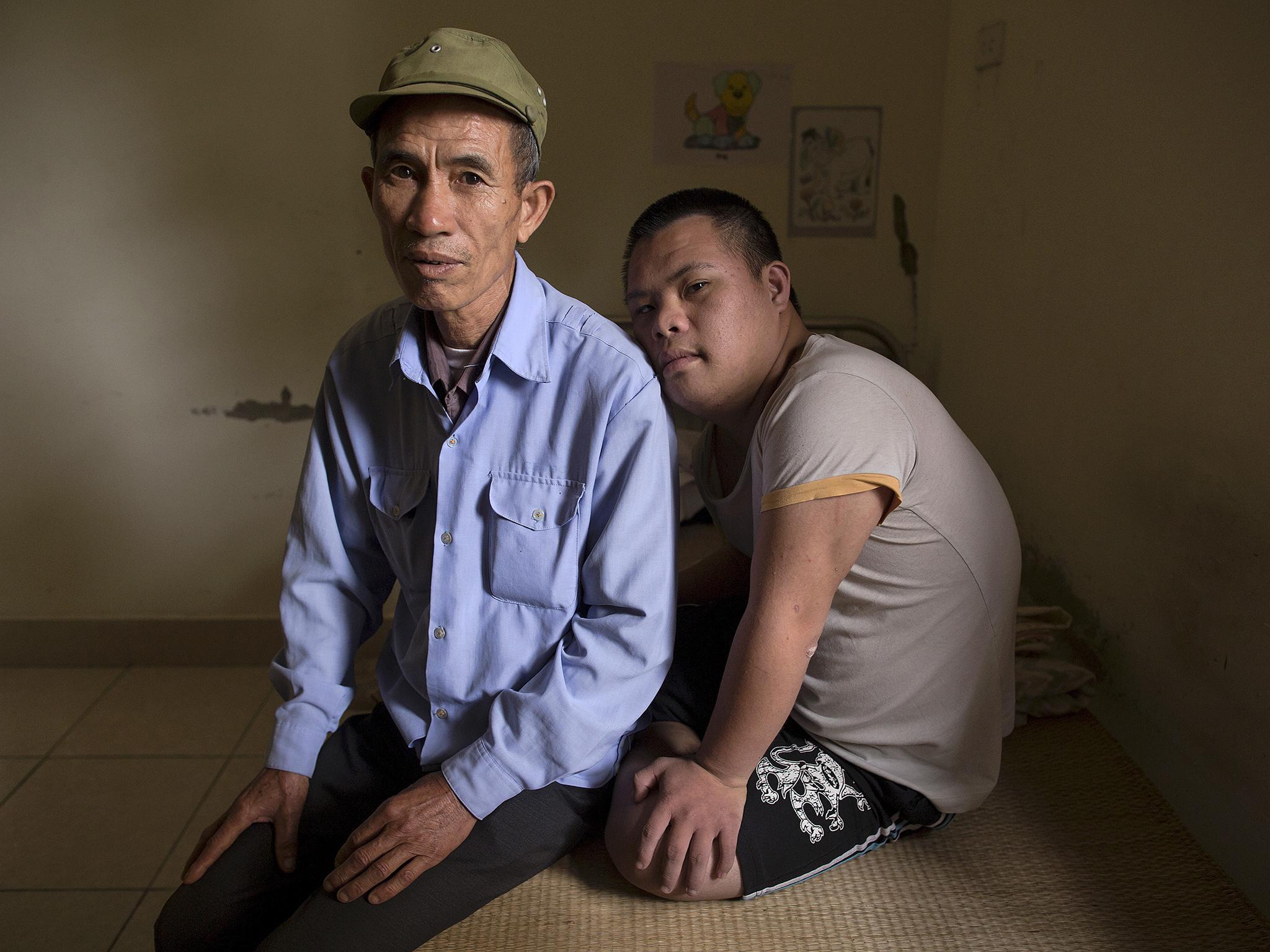 63-year-old former soldier, Nguyen Hong Phuc, sits on the bed with his son Nguyen Dinh Loc, 20, who is recovering from tumour surgery at a hospice for Agent Orange victims (Damir Sagolj/Reuters)