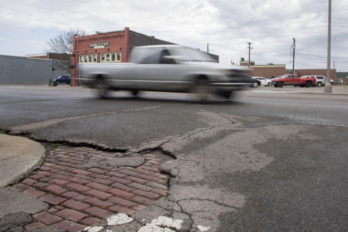 An old brick road surface is exposed where asphalt has broken apart on Main Street