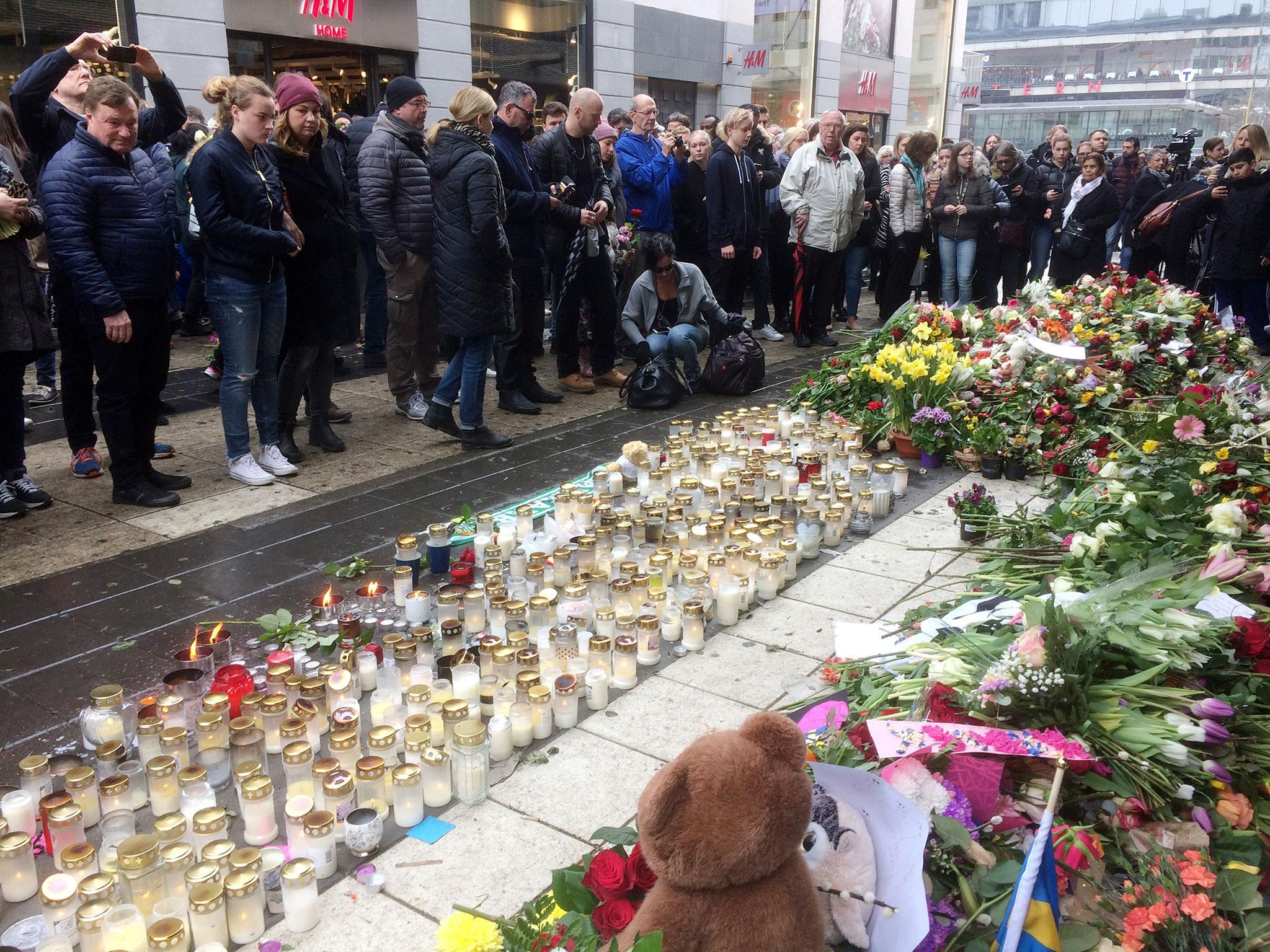 People look at flowers and candles next to the Ahlens department store following the attack in central Stockholm