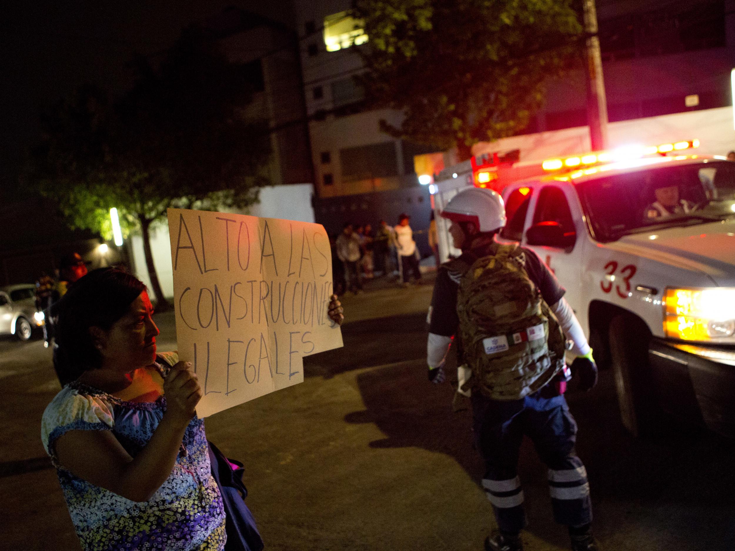 A woman carries a sign reading 'Stop illegal construction' as she protests outside the compound where a parking garage under construction collapsed in Mexico City