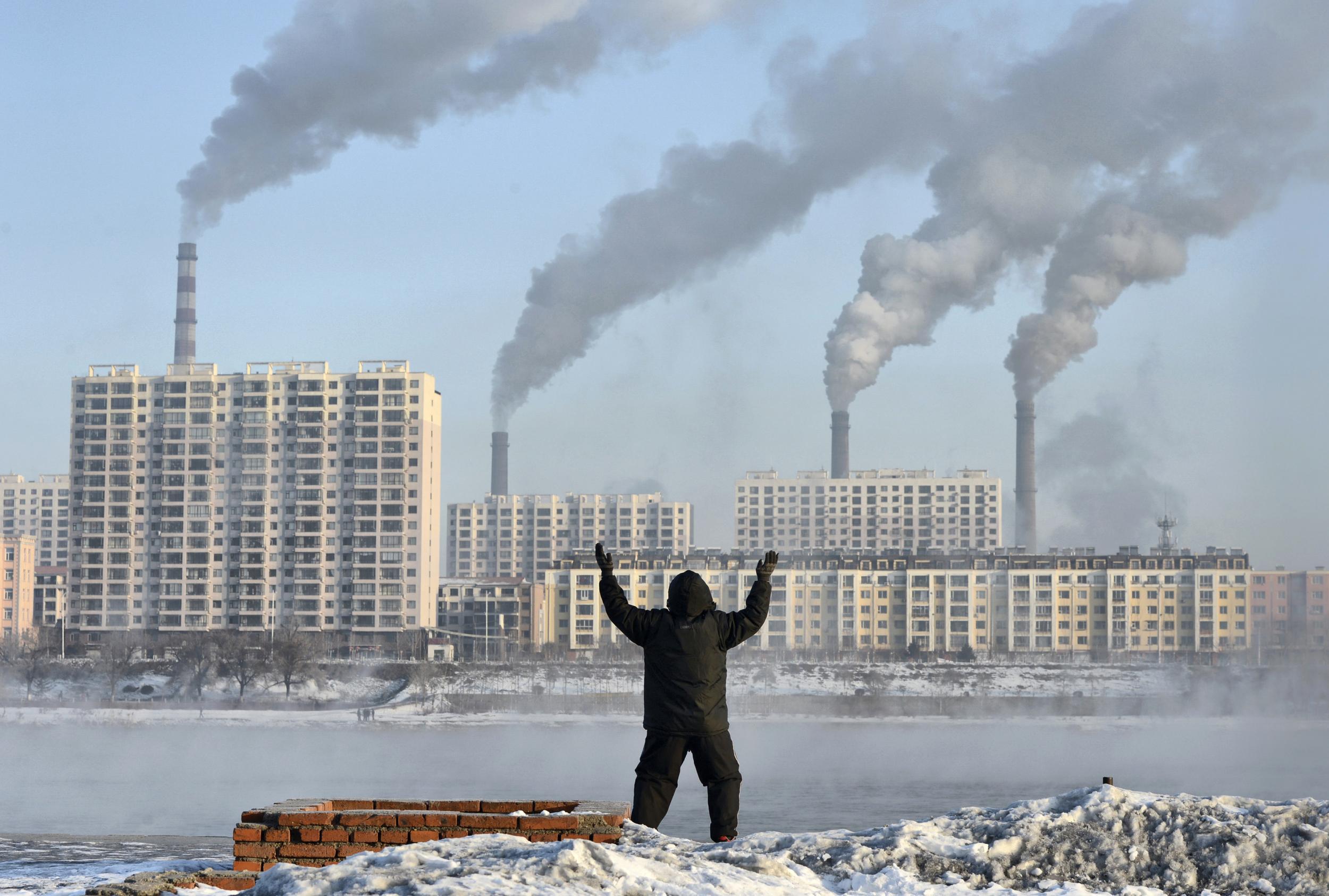 An elderly man exercises on the banks of the Songhua River in Jilin, China, as smoke billows from huge chimneys