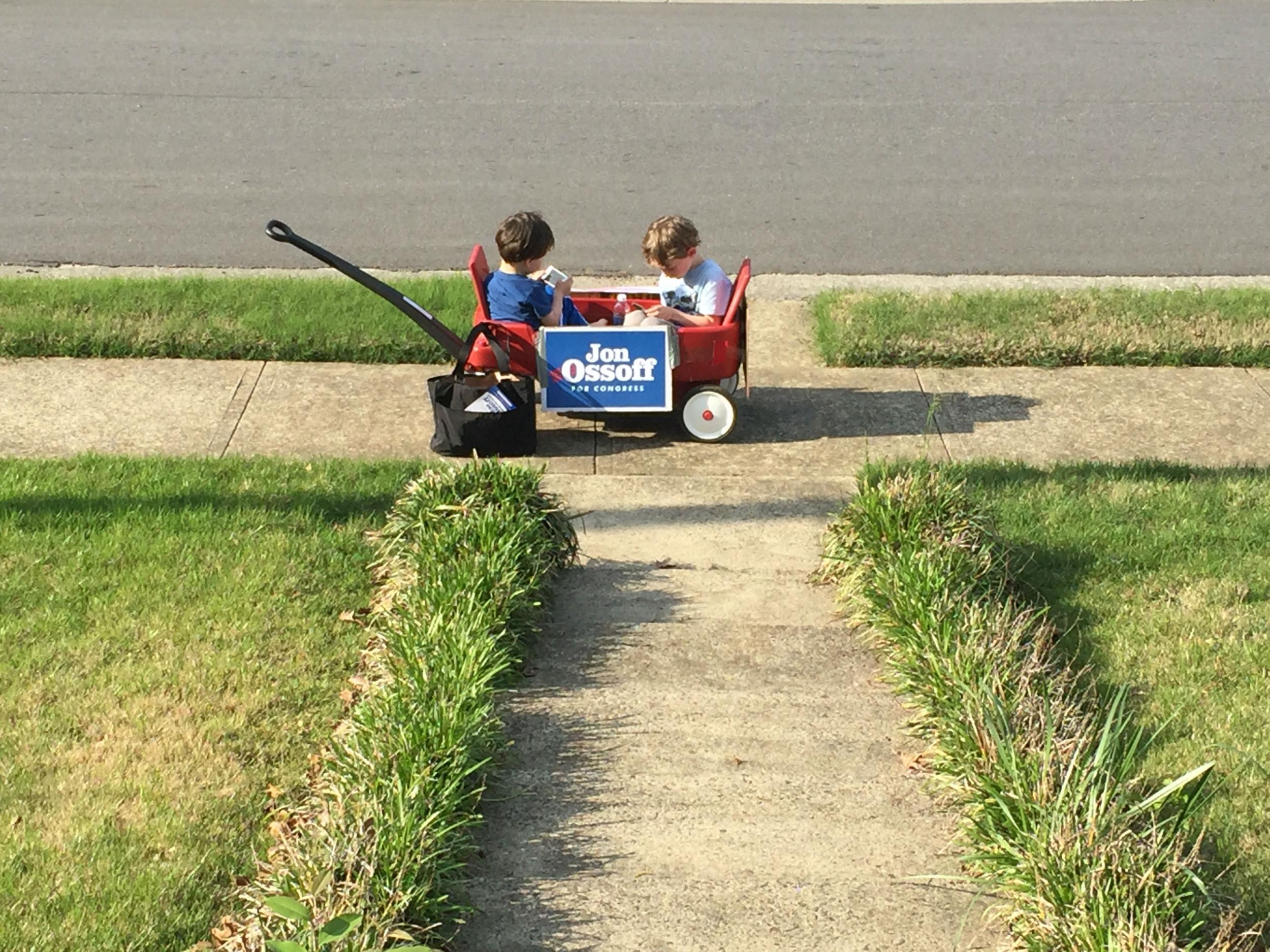 Two very young canvassers going – being pulled – door to door in support of Jon Ossoff