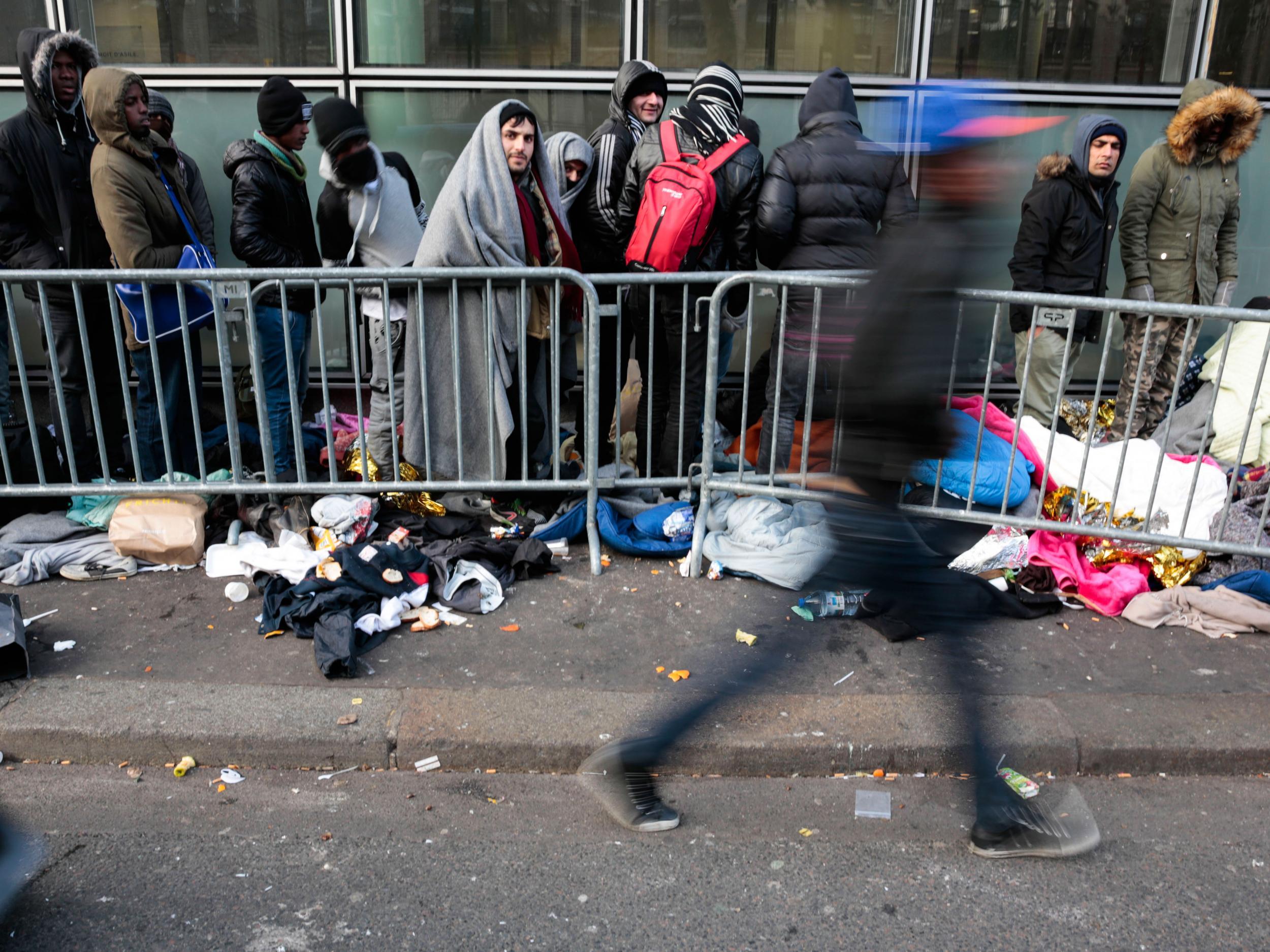 A pedestrian walks by refugees as they queue up outside a centre of an NGO for migrants