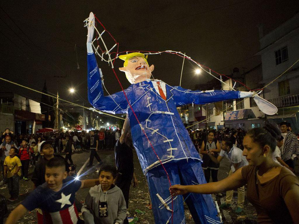 People gather around as a woman prepares to light a figure of Donald Trump rigged with fireworks