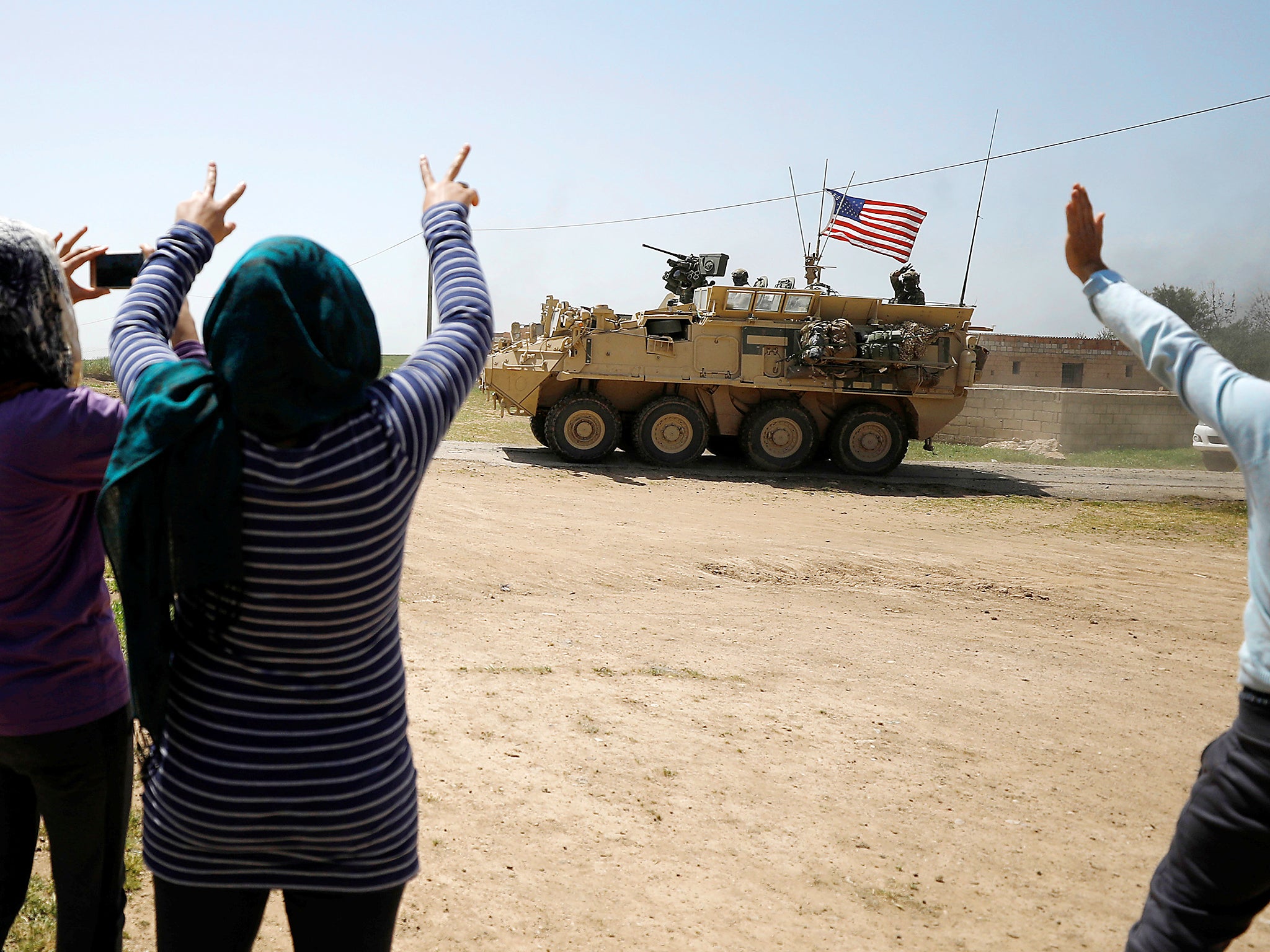 People wave as a US military vehicle travels through Amuda province, northern Syria