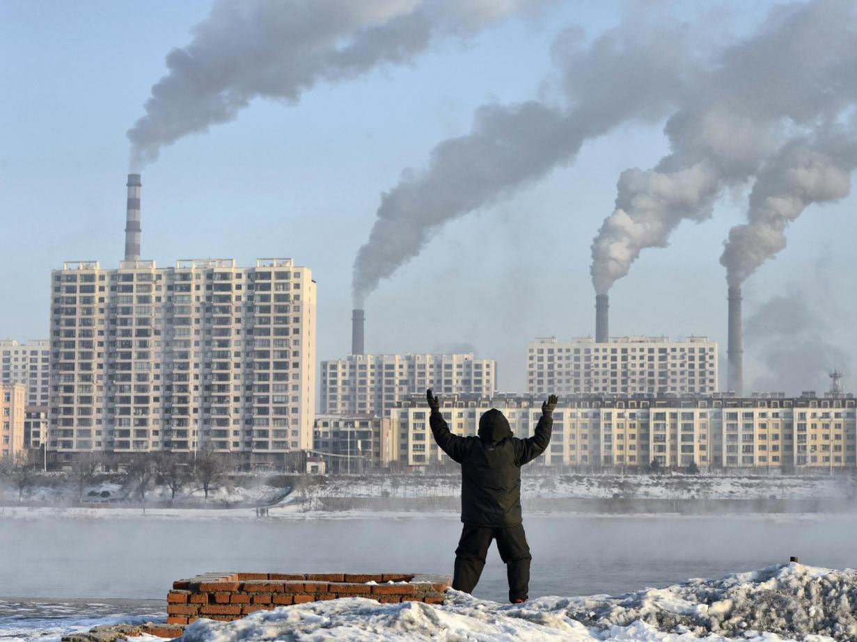 An elderly man exercises on the banks of the Songhua River in Jilin, China, as smoke billows from huge chimneys