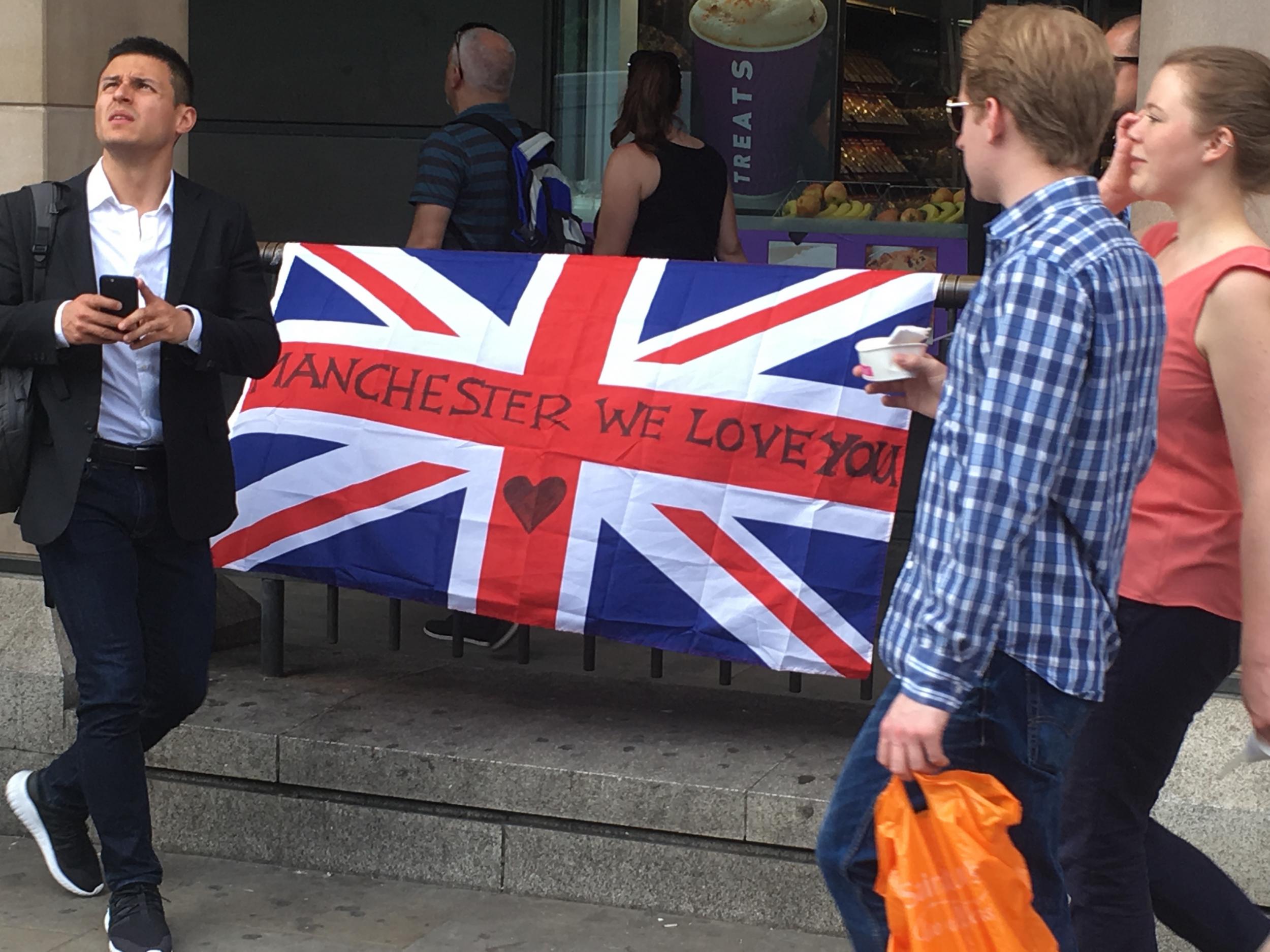 Stand together: Tourists in Westminster pass a flag expressing solidarity with the people of Manchester