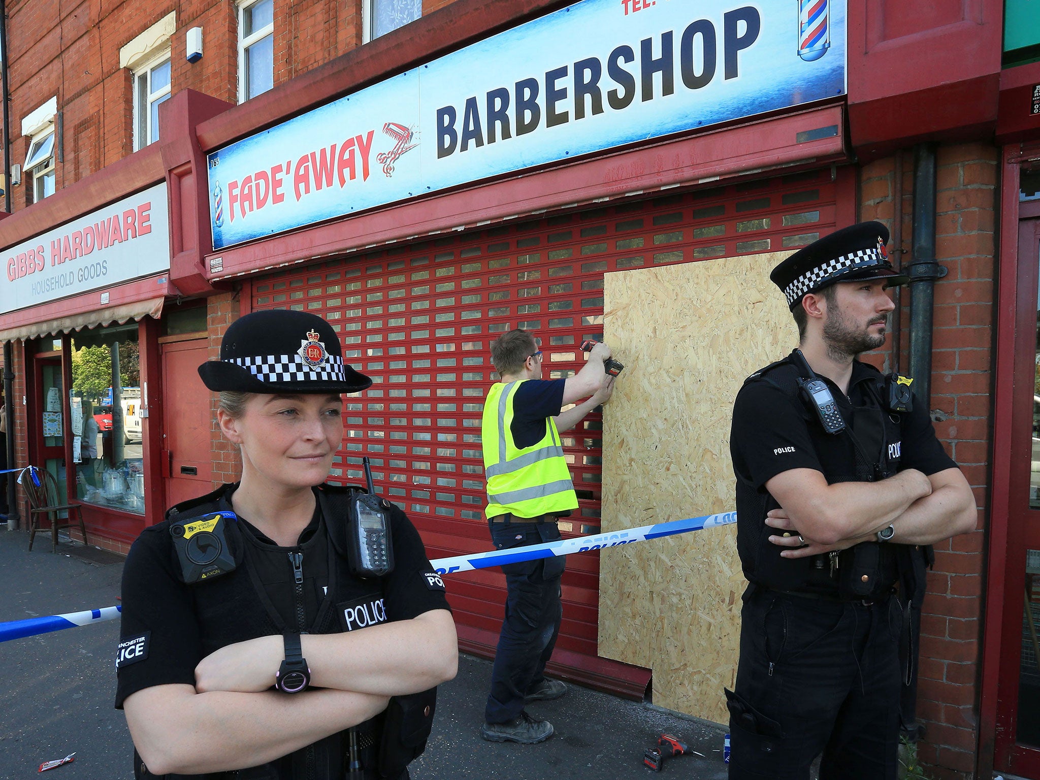 Police stand on duty at the Fade-away barber shop on Princess Road in Moss Side, Manchester, on 26 May