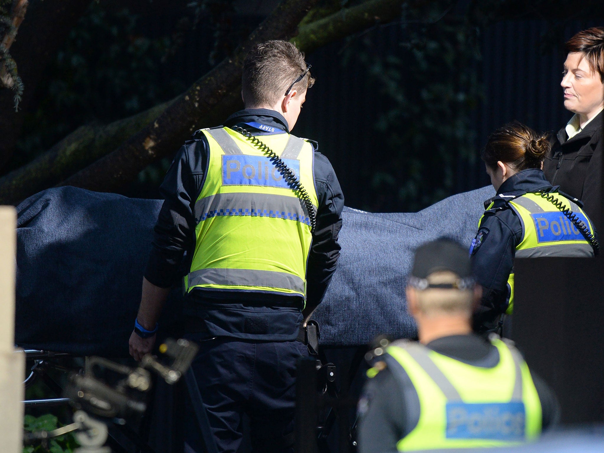 Police officers help the coroner remove a body at the scene of a hostage situation in the Melbourne bayside suburb of Brighton on June 6, 2017