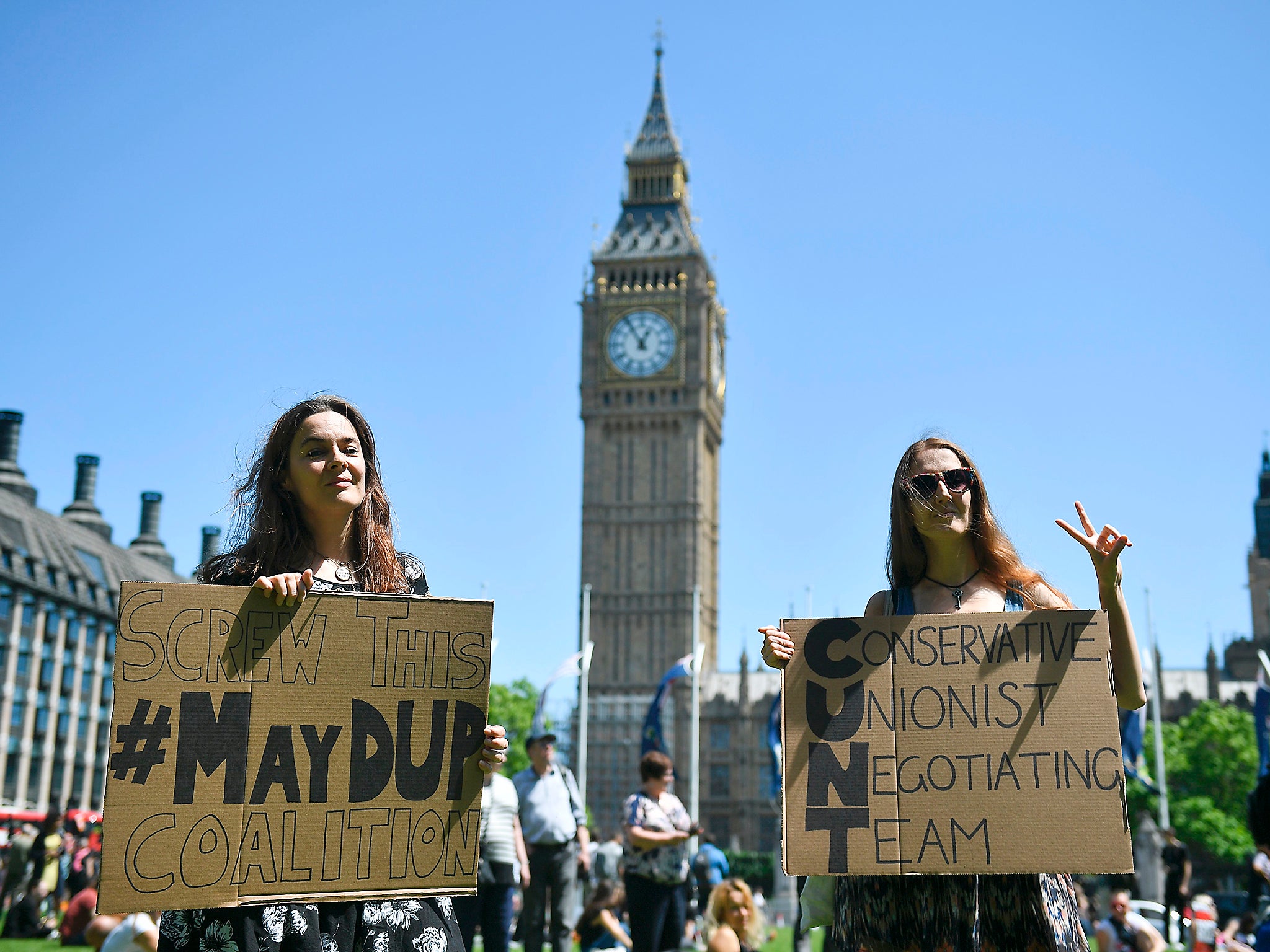 Anti-Conservative Party and anti-Democratic Unionist Party (DUP) demonstrators pose with placards in Parliament Square in front of the Houses of Parliament in central London